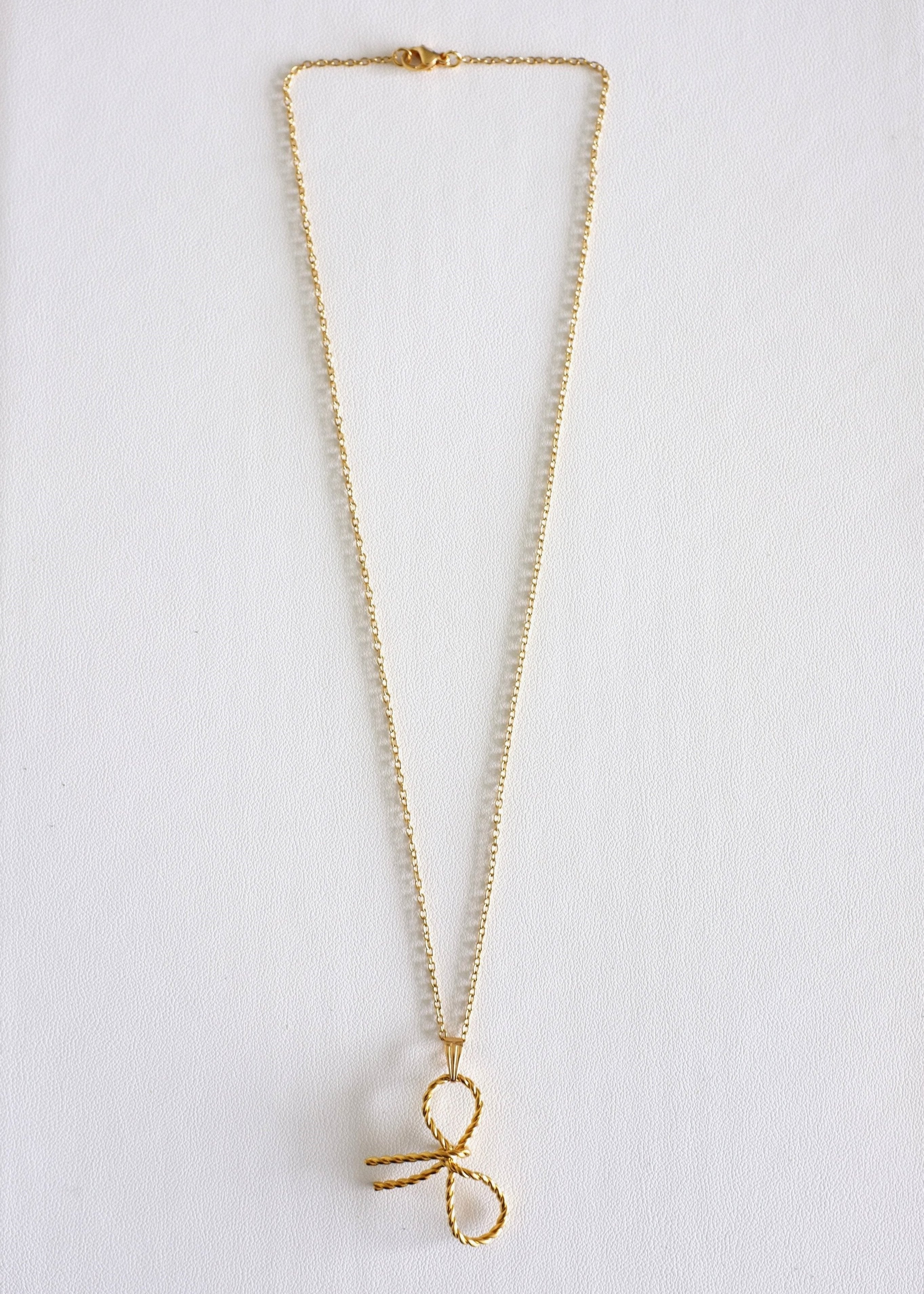 A gold-colored stainless steel necklace with a delicate bow pendant on a white background.