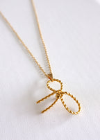 A gold-colored stainless steel necklace with a delicate bow pendant on a white background.
