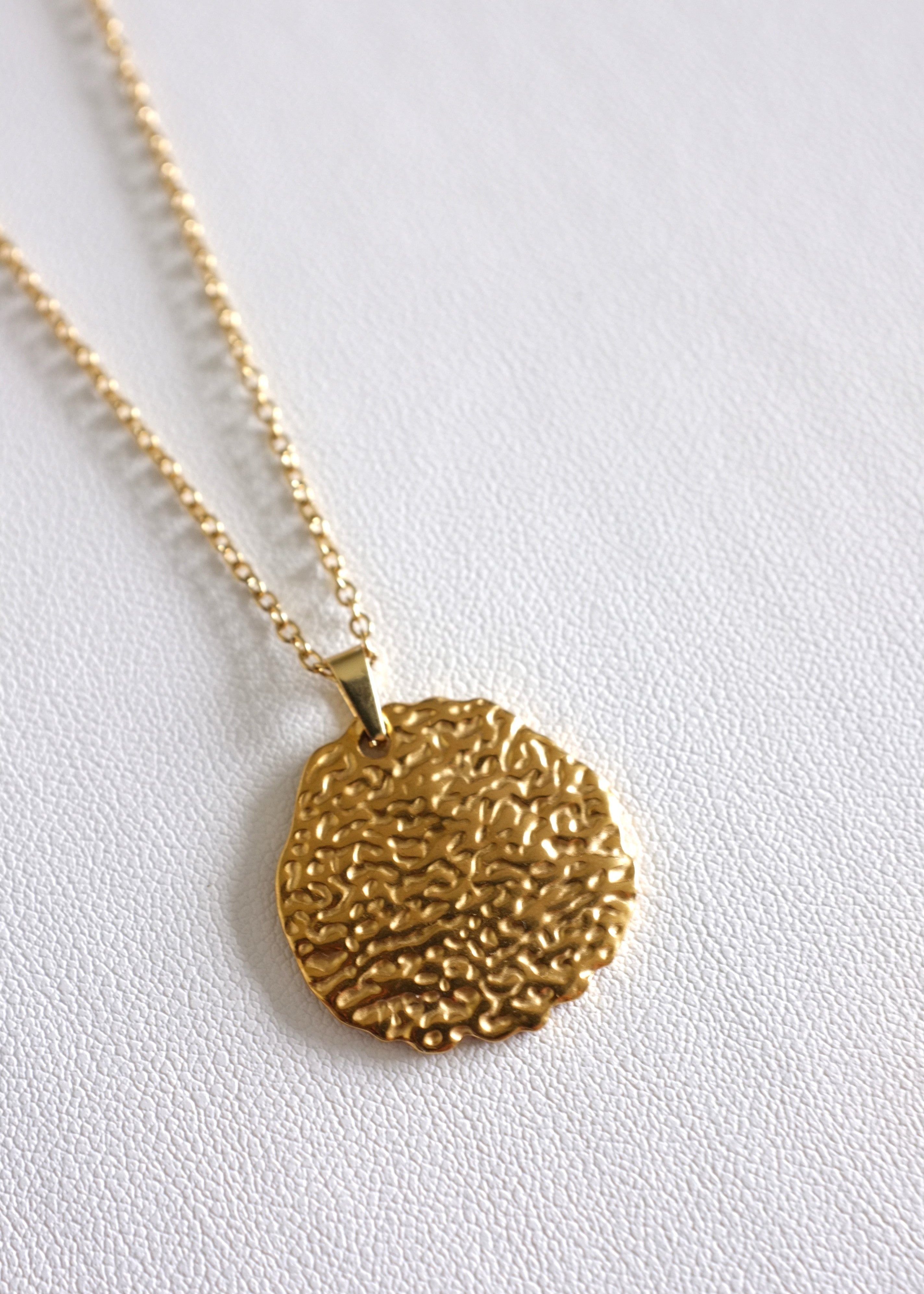 A gold stainless steel crater pendant on a chain, displayed on a white background.