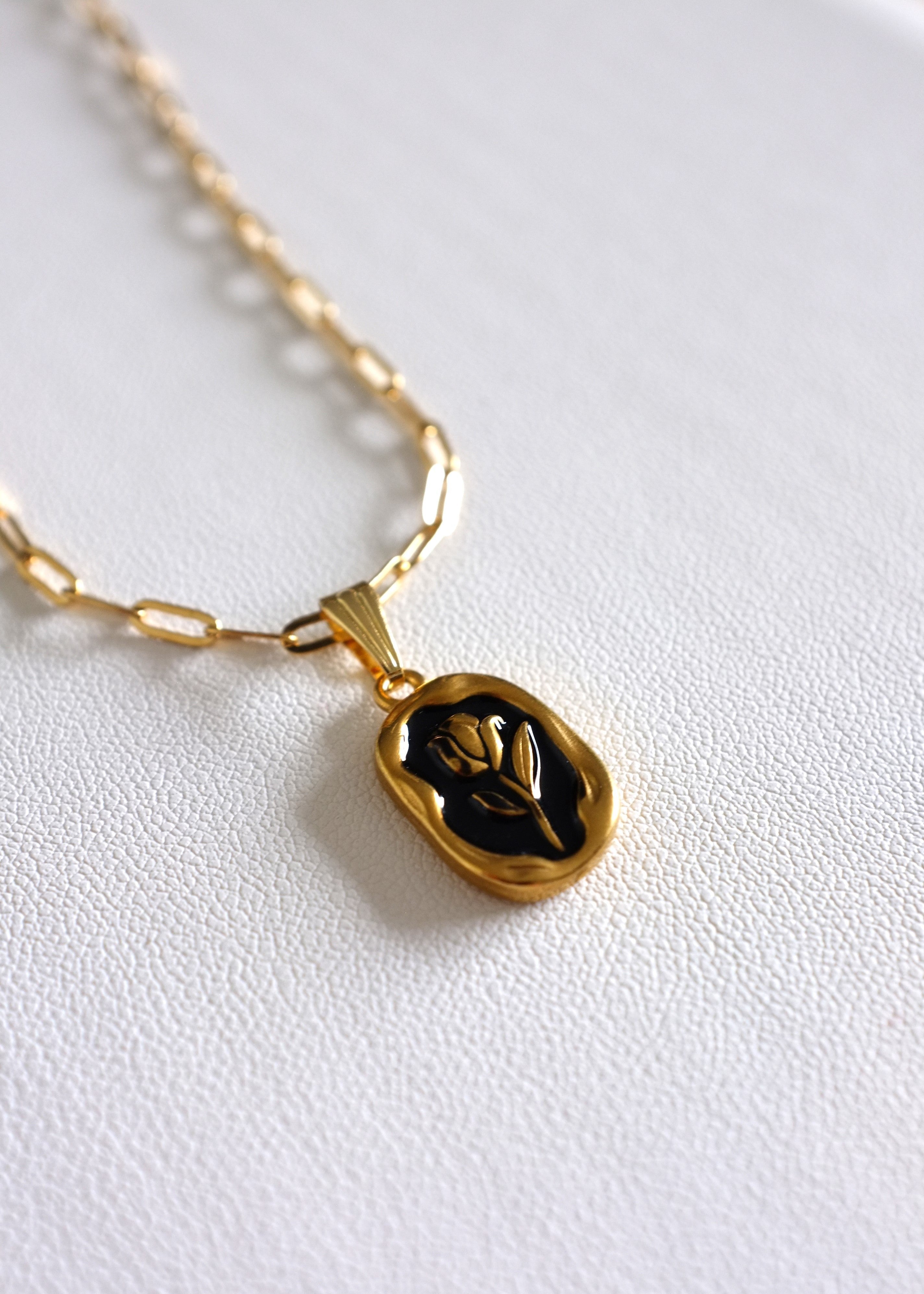 close up of gold stainless steel paperclip chain with a back enamel tulip charm on white background
