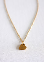 close up of gold stainless steel chain with a small stamped heart charm on white background