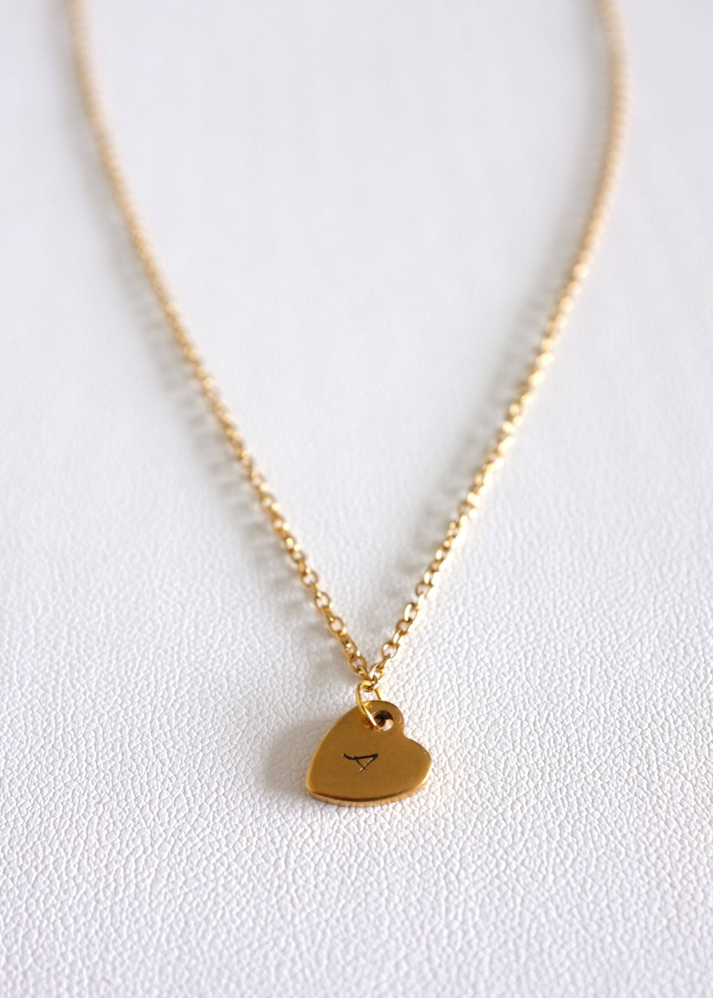 close up of gold stainless steel chain with a small stamped heart charm on white background