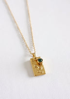 A stainless steel necklace with a unique rectangular pendant featuring a vibrant green gem, displayed against a white background.