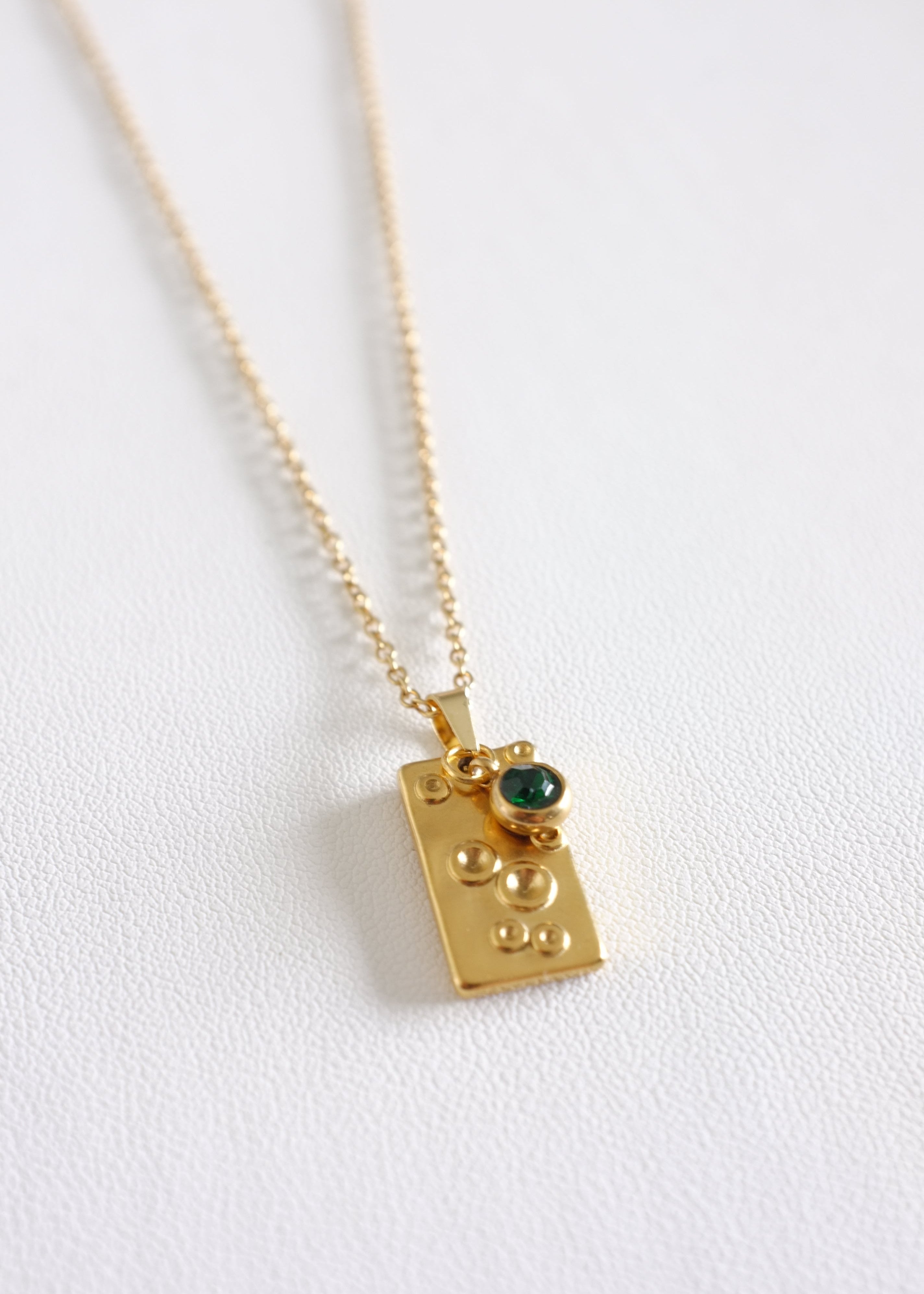 A stainless steel necklace with a unique rectangular pendant featuring a vibrant green gem, displayed against a white background.