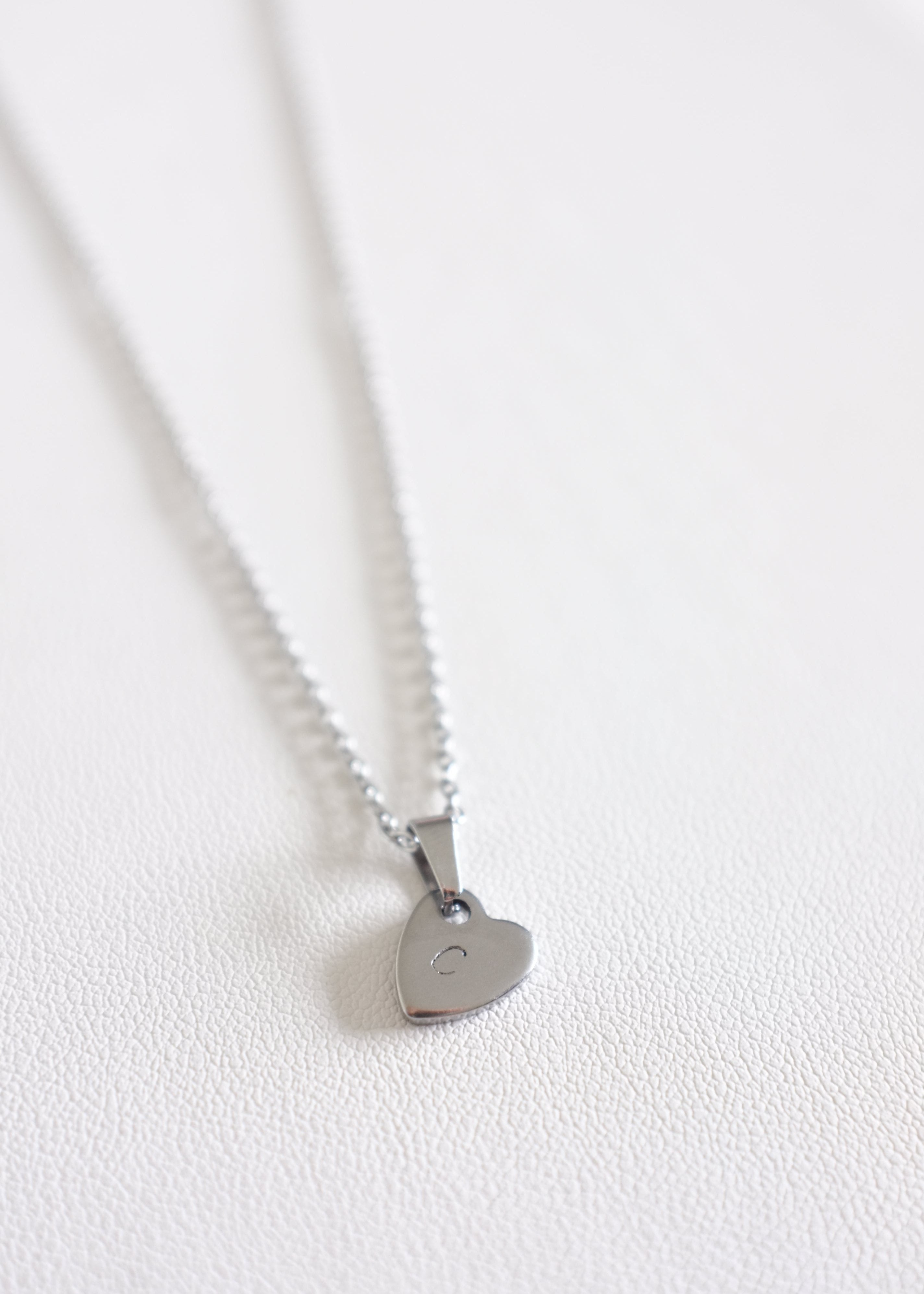 close up of silver stainless steel chain with a small stamped heart charm on white background