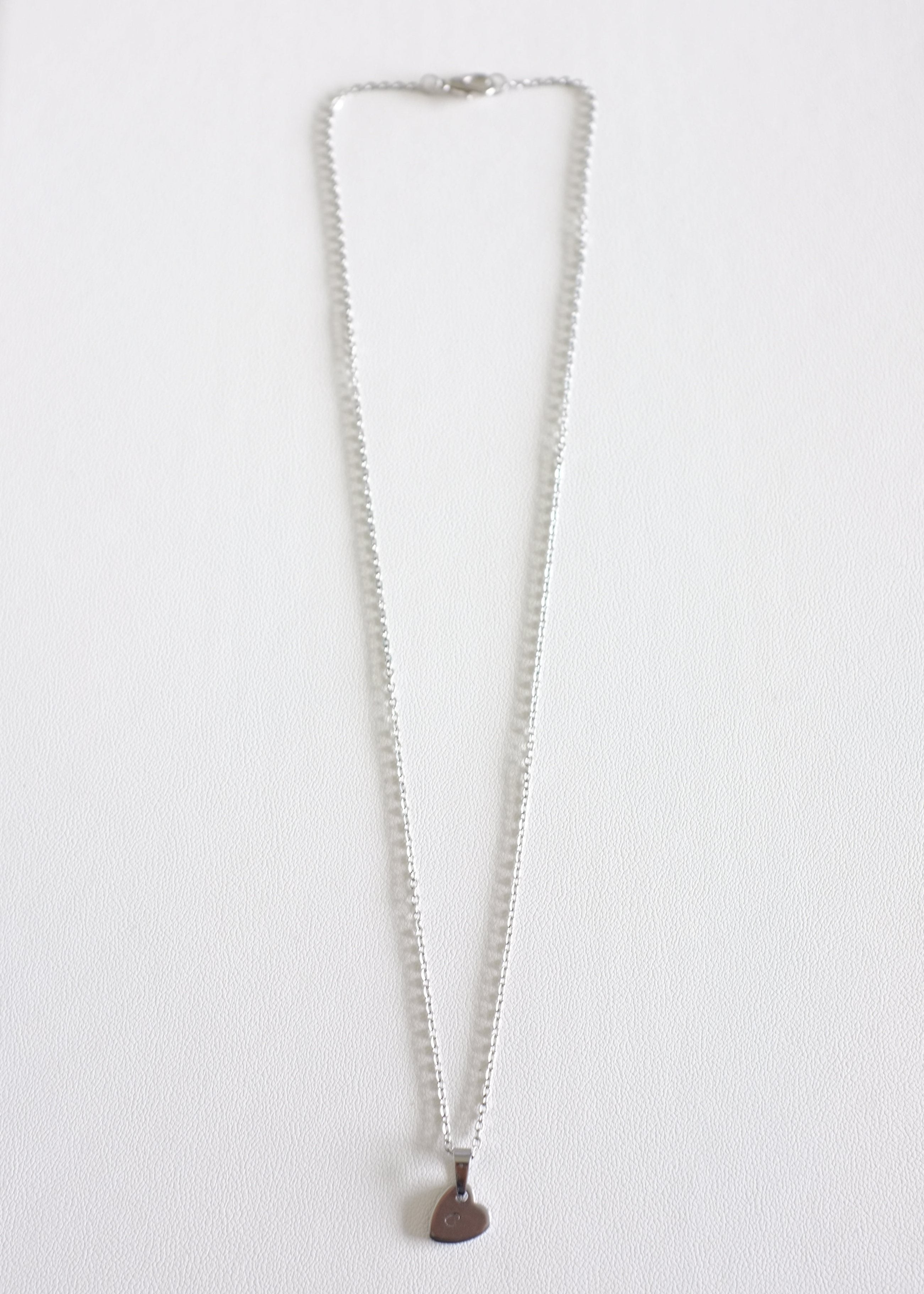 silver stainless steel chain with a small stamped heart charm on white background