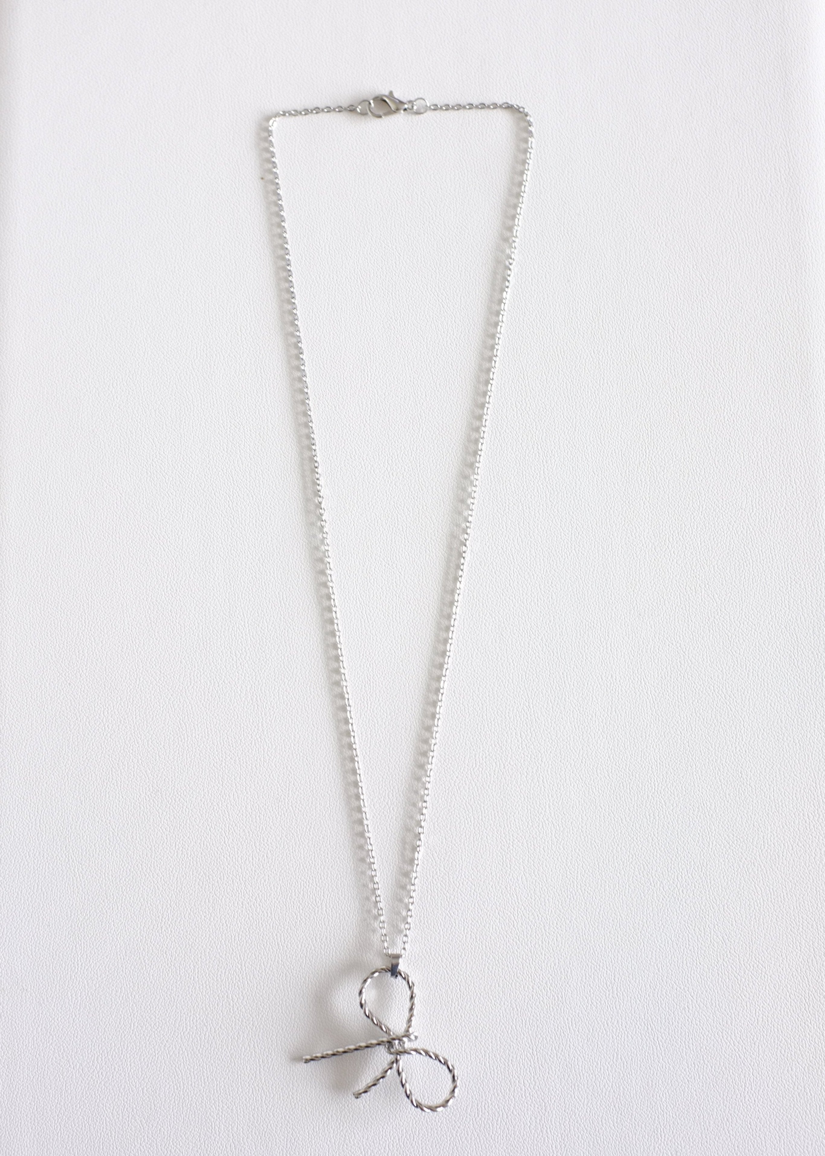 A silver-colored stainless steel necklace with a delicate bow pendant on a white background.