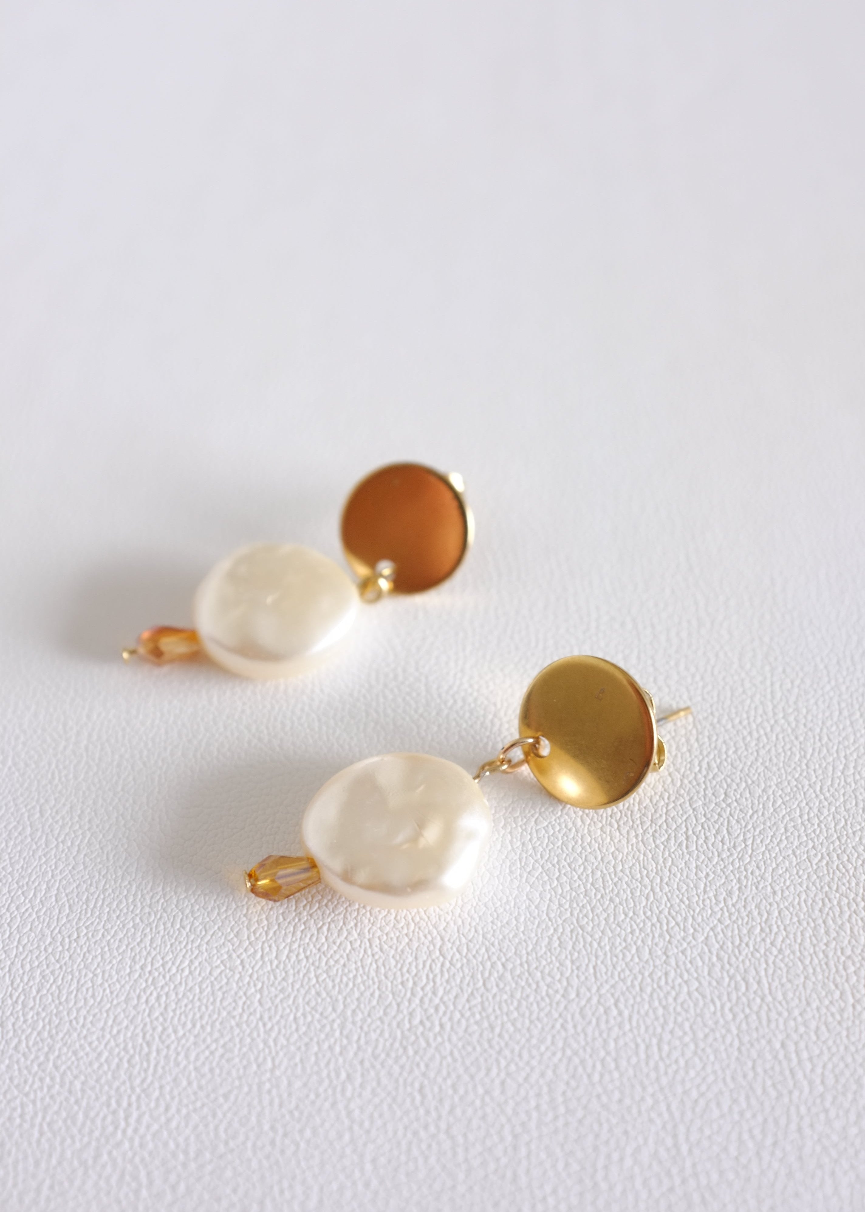 A pair of stainless steel hoop earrings with pearl shell design, displayed against a white background.