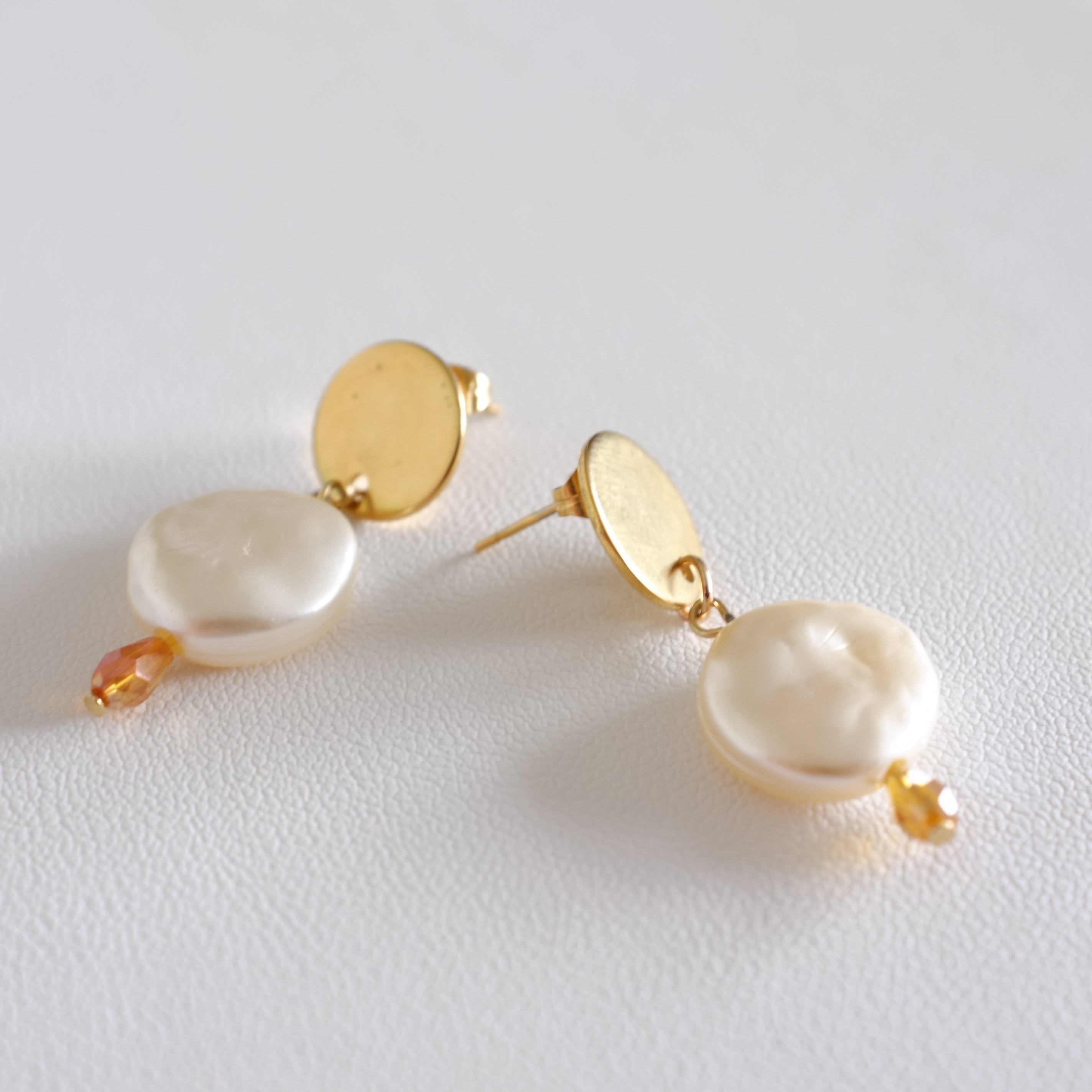 close up of a pair of stainless steel hoop earrings with pearl shell design, displayed against a white background.