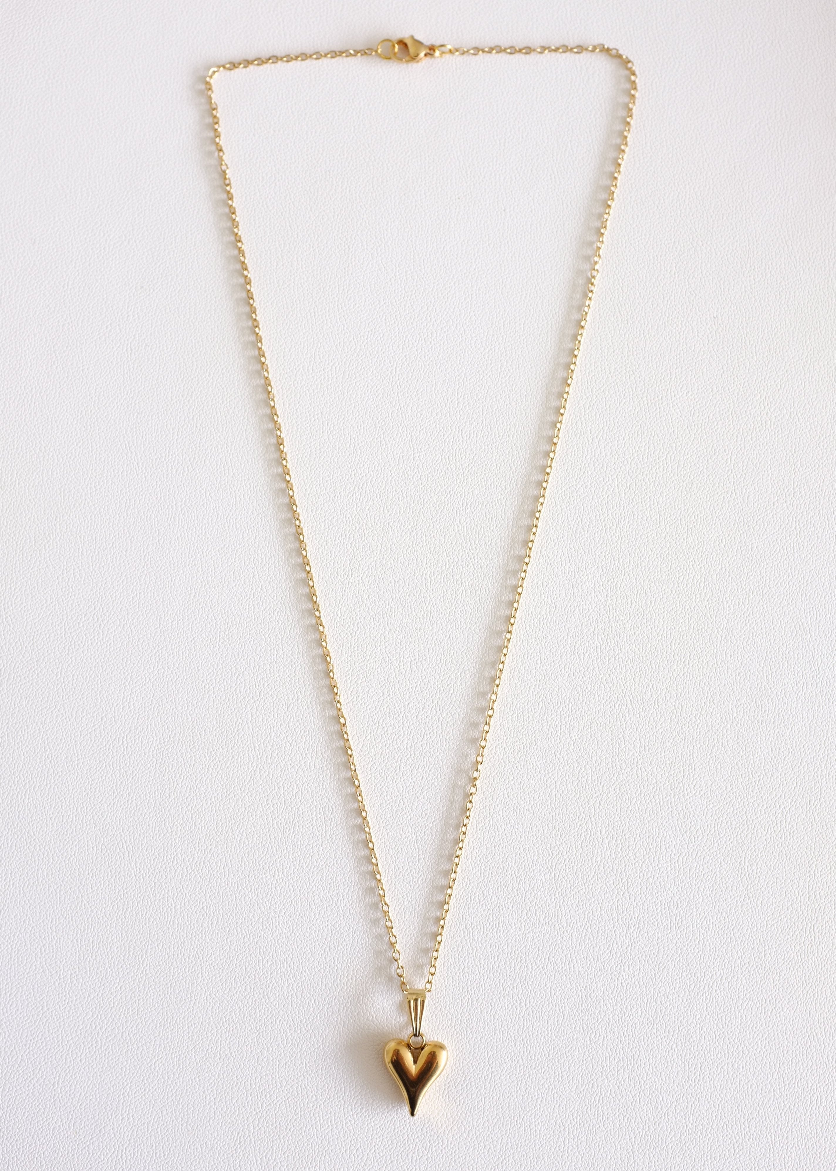 A gold-colored stainless steel necklace with a heart-shaped pendant, displayed on a white background.