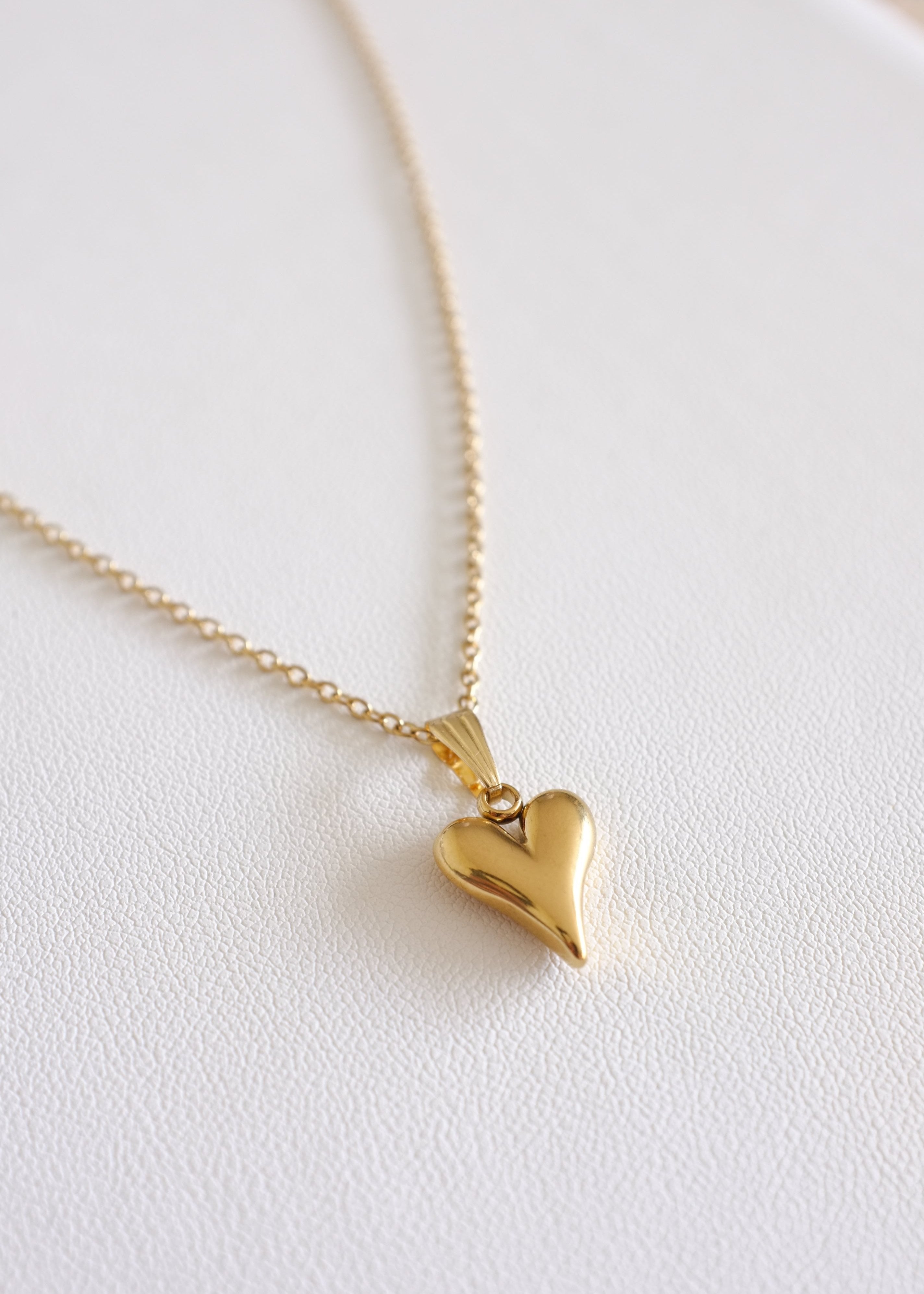 A gold-colored stainless steel necklace with a heart-shaped pendant, displayed on a white background.