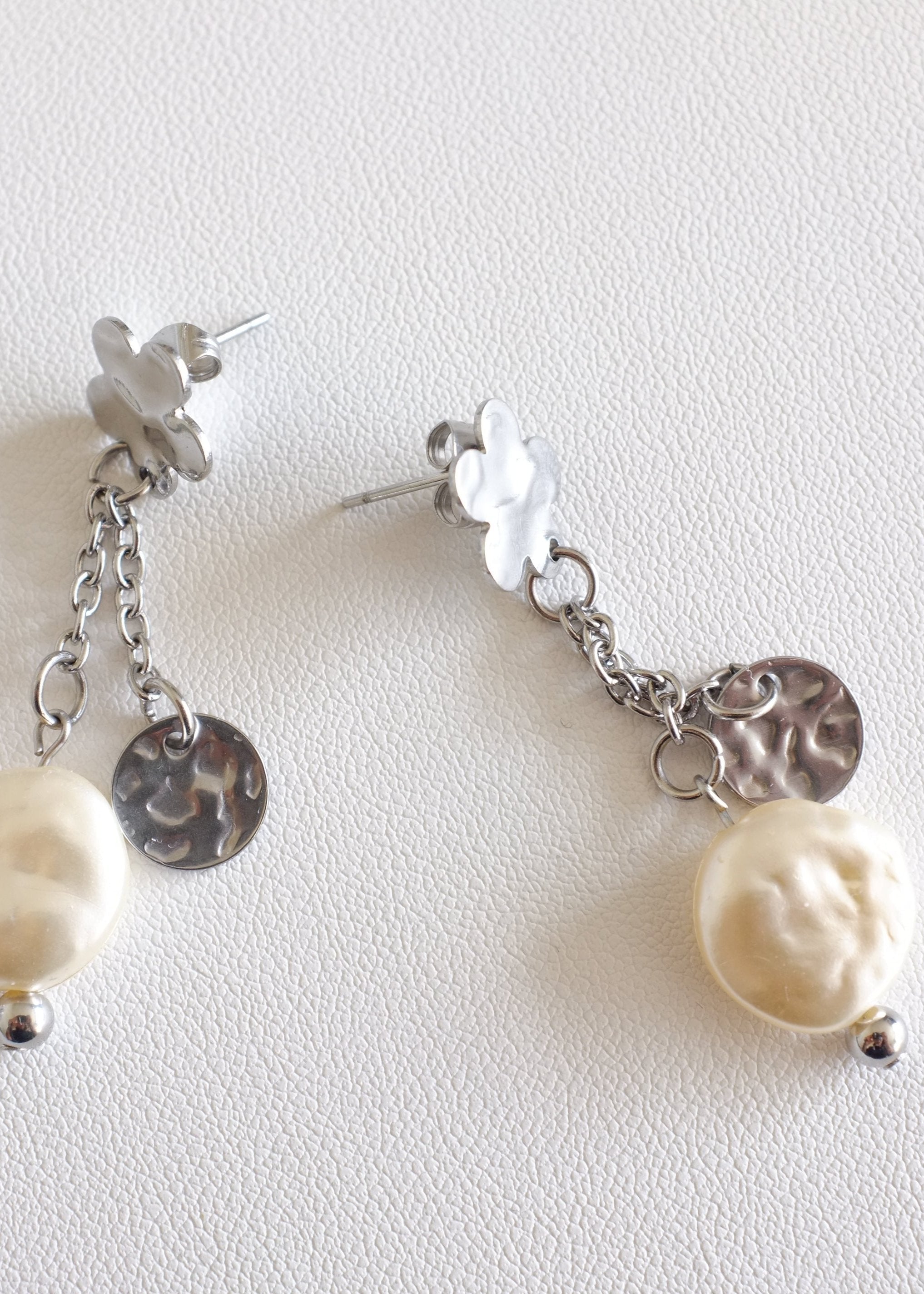 A pair of silver-colored floral stud earrings with a flat imitation pearl and a small pendant attached to two dainty chains.