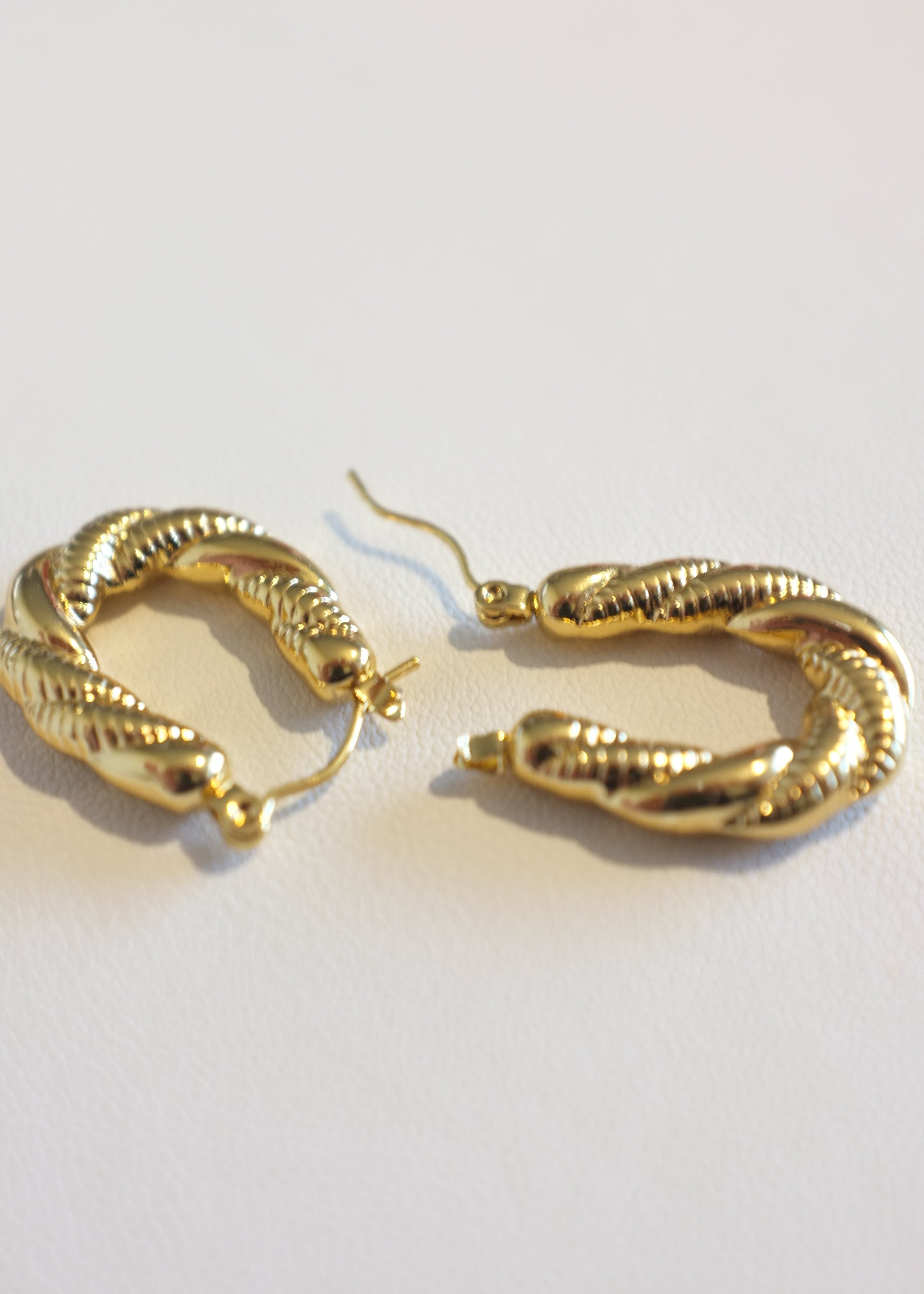 A pair of gold-colored stainless steel hoop earrings with a twisted rope design, displayed against a white background.