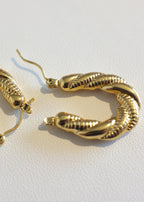 close up of a  pair of gold-colored stainless steel hoop earrings with a twisted rope design, displayed against a white background.