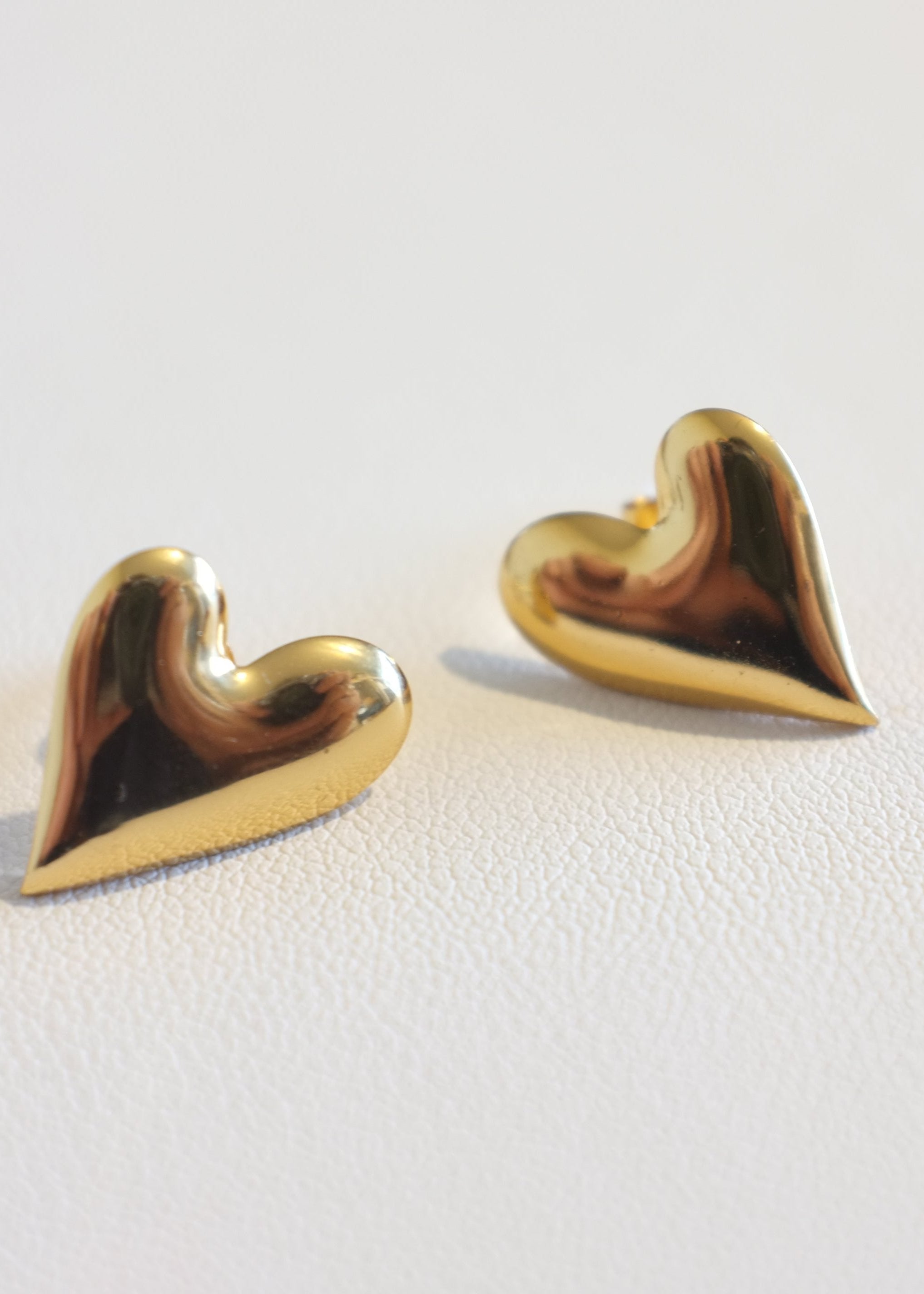 A pair of gold-colored heart-shaped stud earrings on a white background.