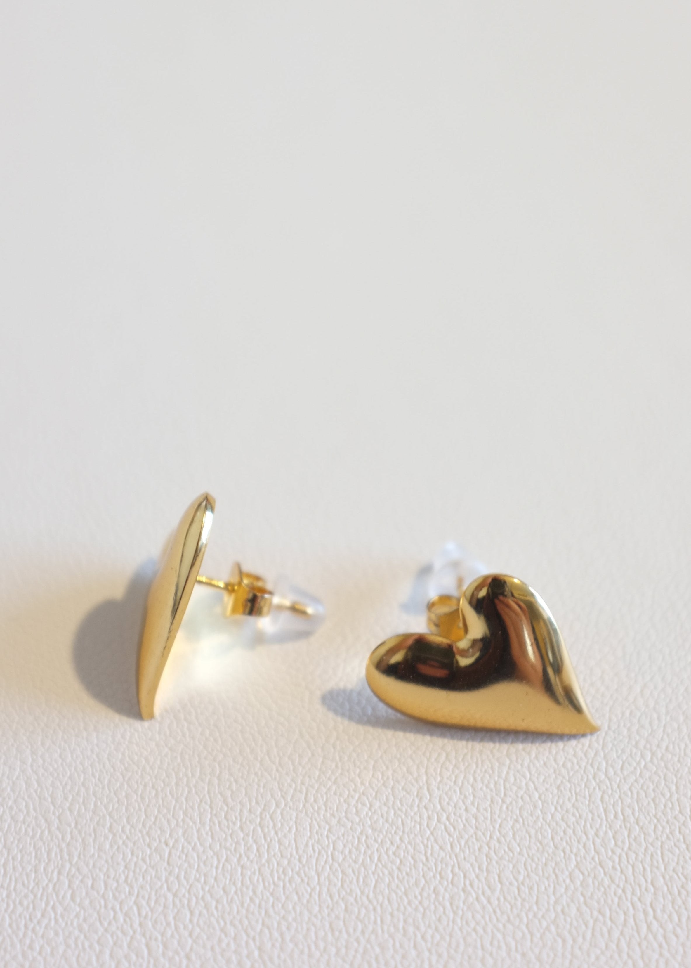 A pair of gold-colored heart-shaped stud earrings on a white background.