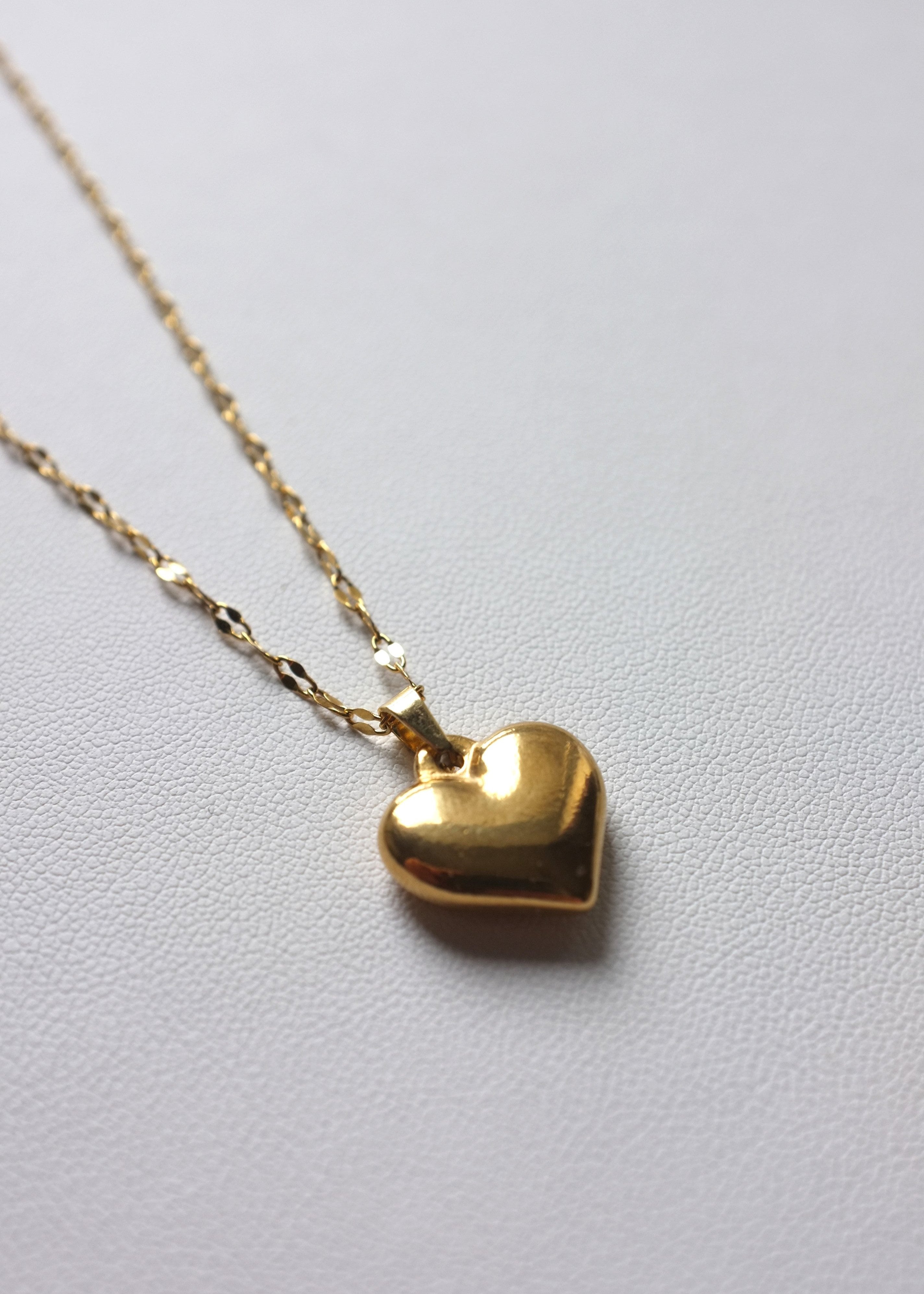 A gold-colored heart-shaped pendant necklace with a thin stainless steel chain.