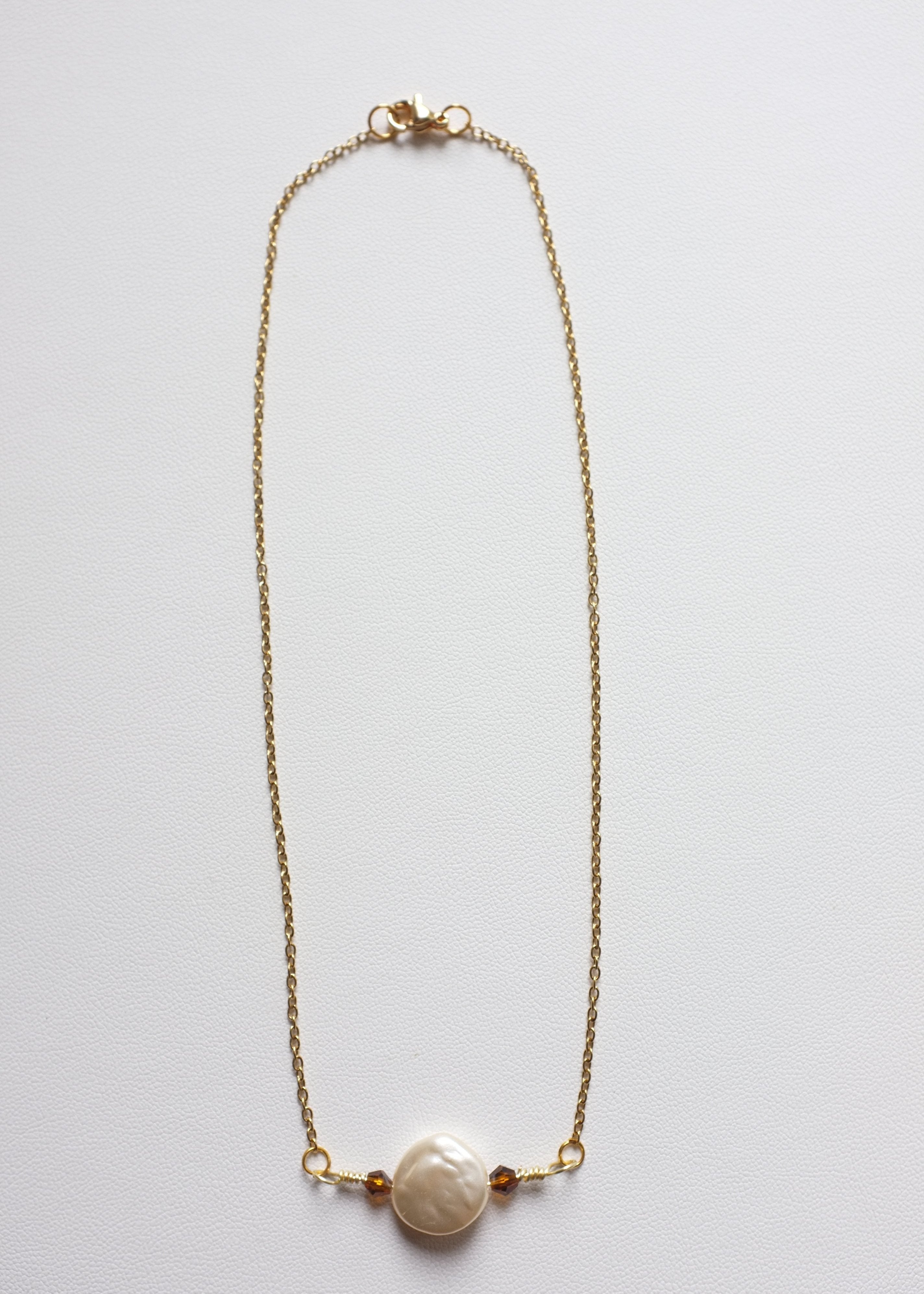A stainless steel necklace with a flat imitation pearl and glass bead centerpiece, featuring a gold-tone chain.