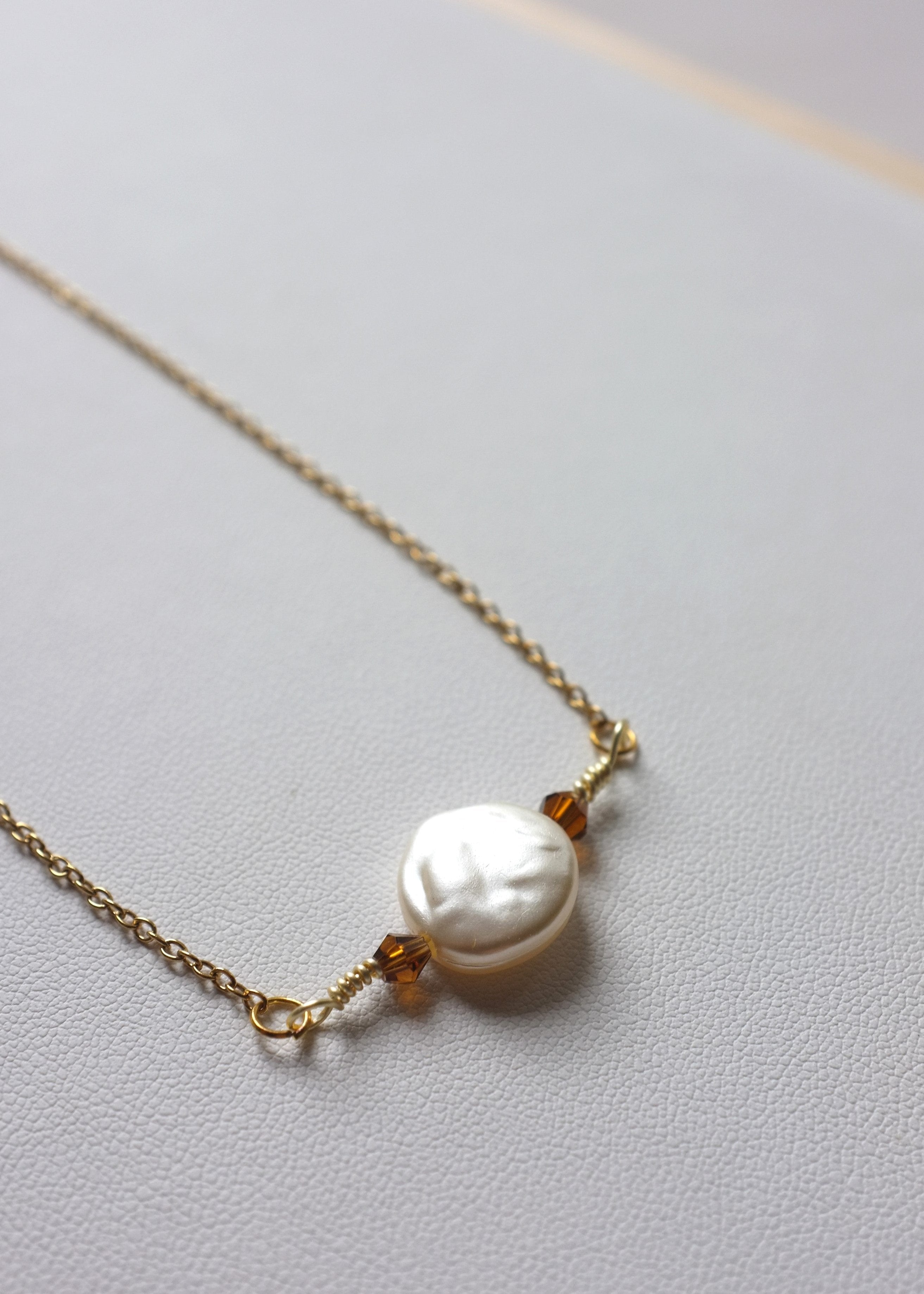 A stainless steel necklace with a flat imitation pearl and glass bead centerpiece, featuring a gold-tone chain.