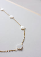 close up of a stainless steel chain necklace with freshwater shell flower beads, featuring a gold-tone chain and white beads.