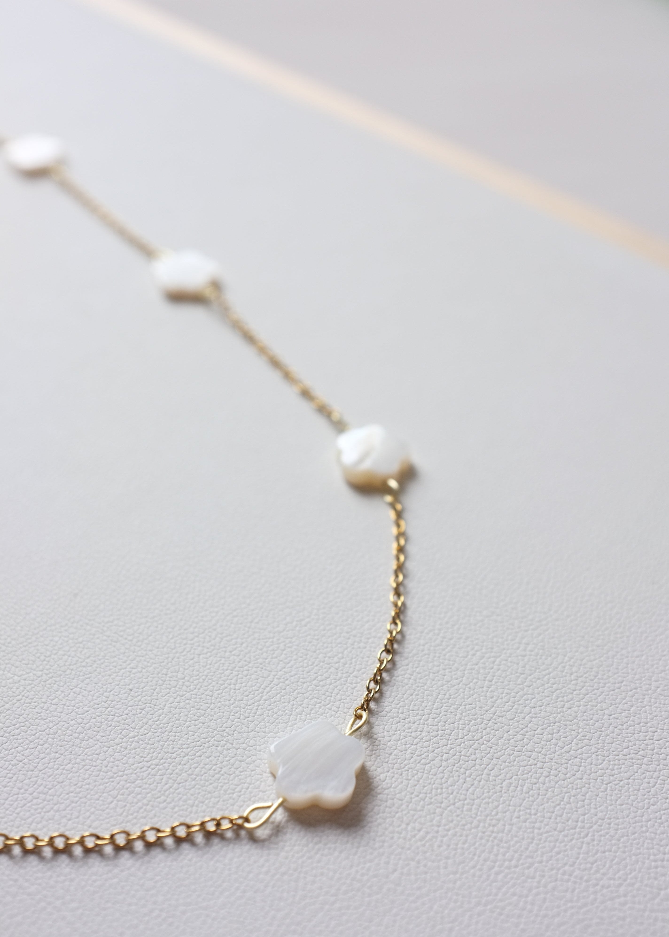 close up of a stainless steel chain necklace with freshwater shell flower beads, featuring a gold-tone chain and white beads.