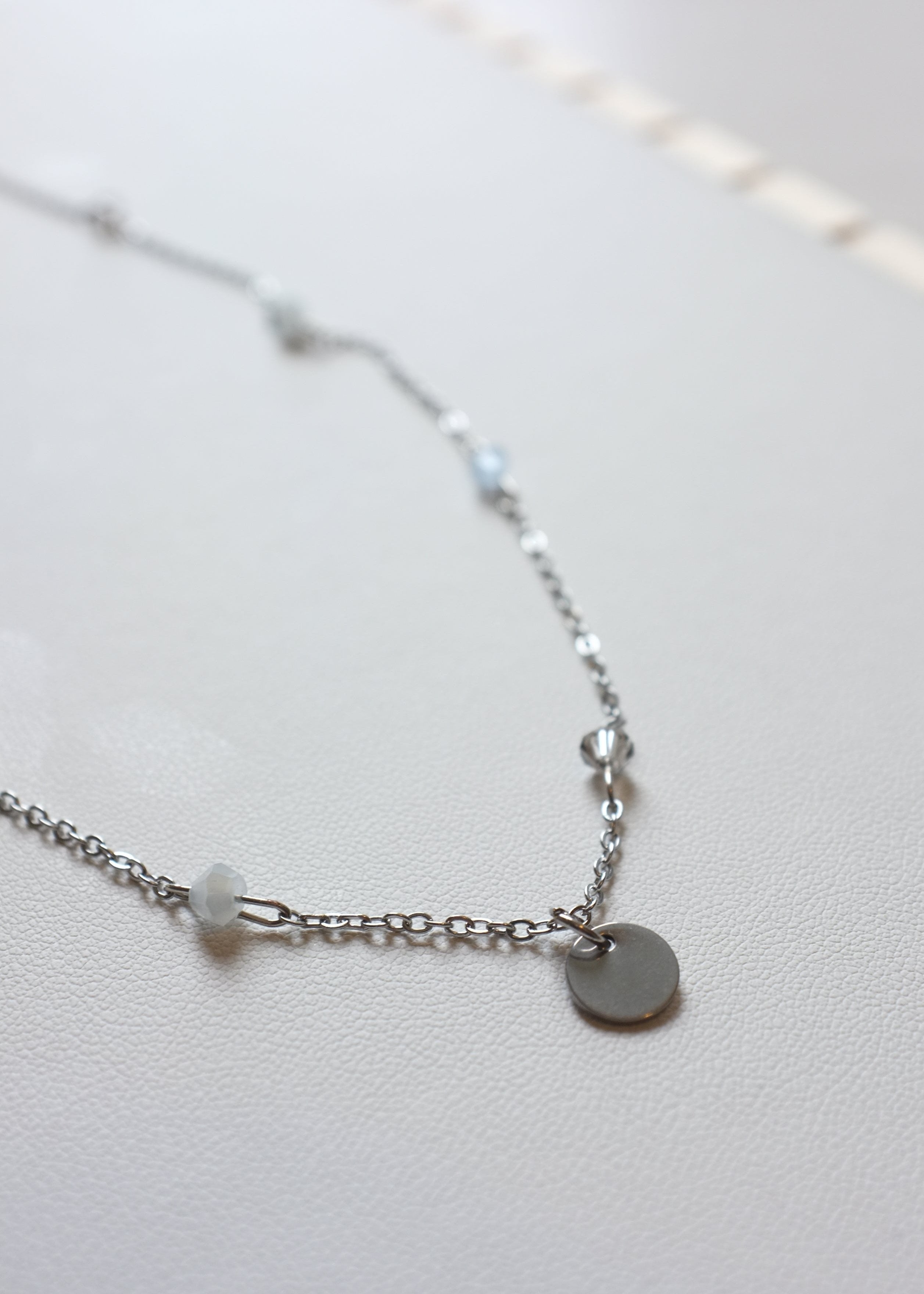 Asilver-colored stainless steel chain necklace with multicolor bicone glass beads and a round engravable pendant.