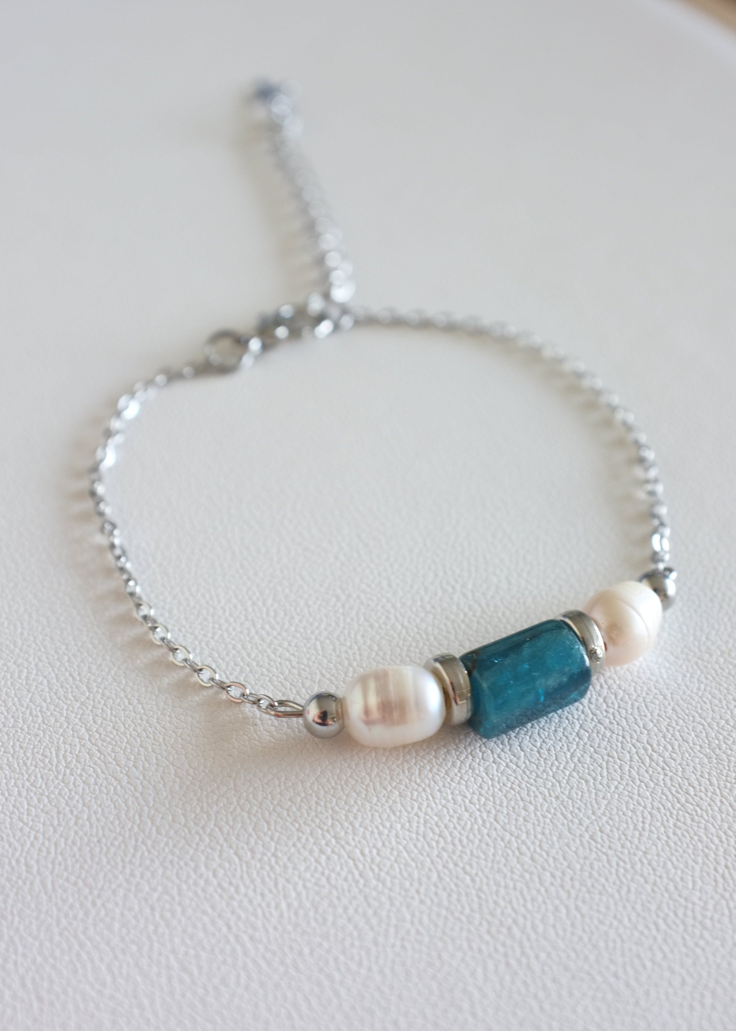 A stainless steel bracelet with two freshwater pearls and a natural stone bead on a white background.