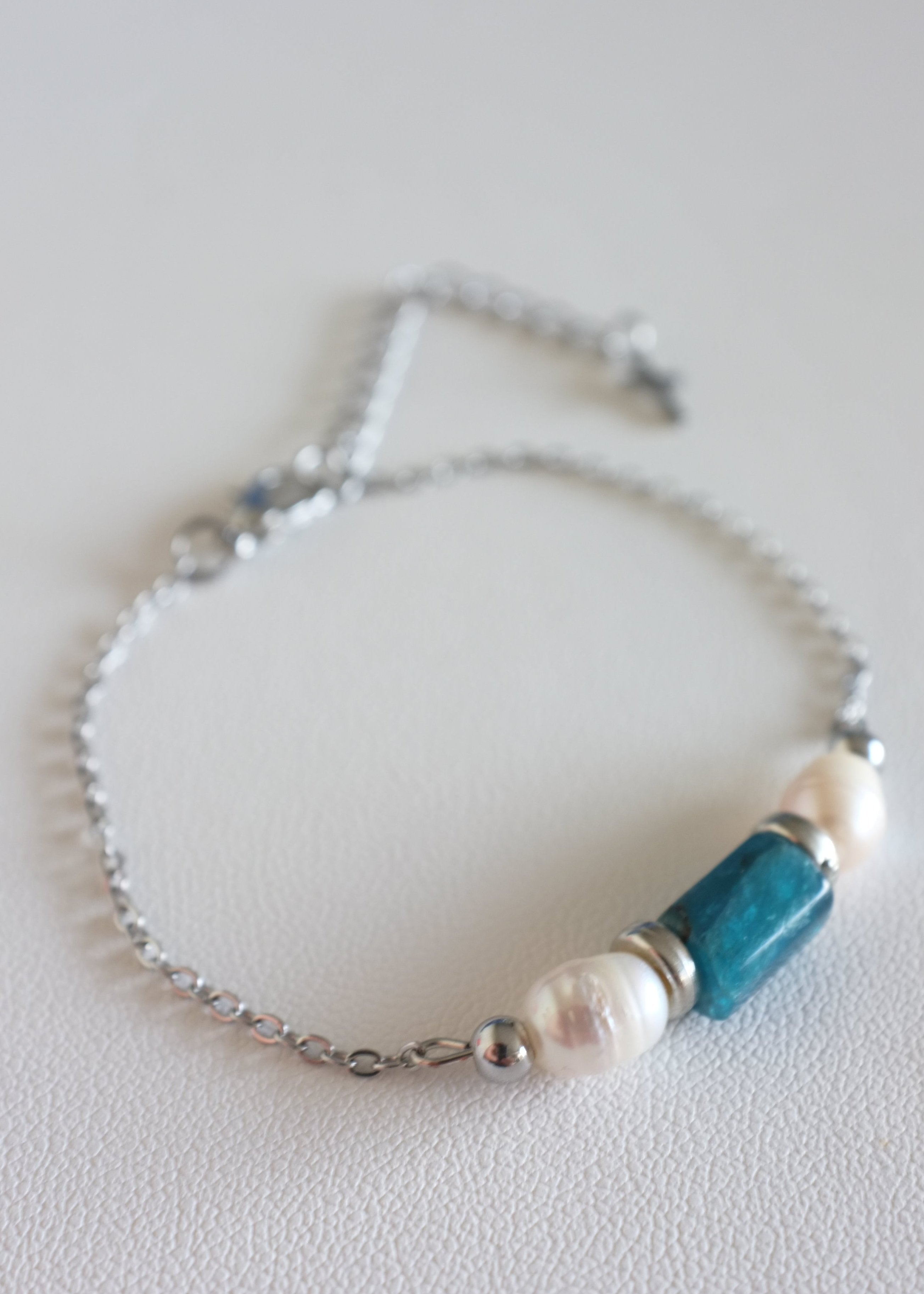 close up of a stainless steel bracelet with two freshwater pearls and a natural stone bead on a white background.