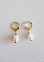 A pair of gold-colored stainless steel hoop earrings with freshwater pearl adornments on a white background