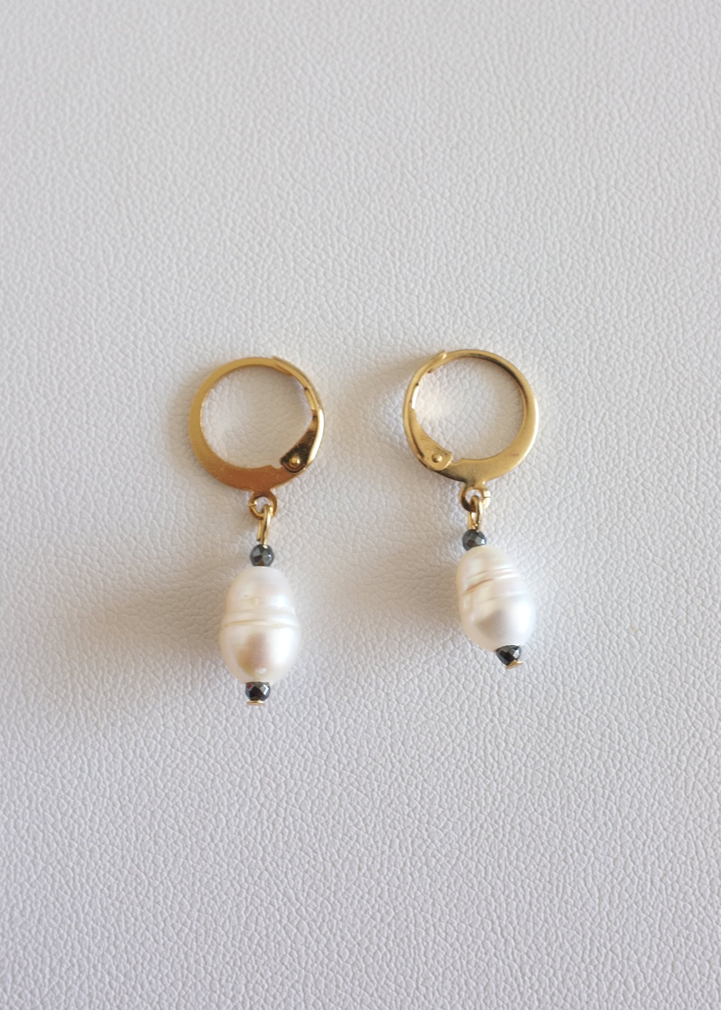 A pair of gold-colored stainless steel hoop earrings with freshwater pearl adornments on a white background