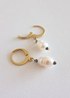 A pair of gold-colored stainless steel hoop earrings with freshwater pearl adornments.