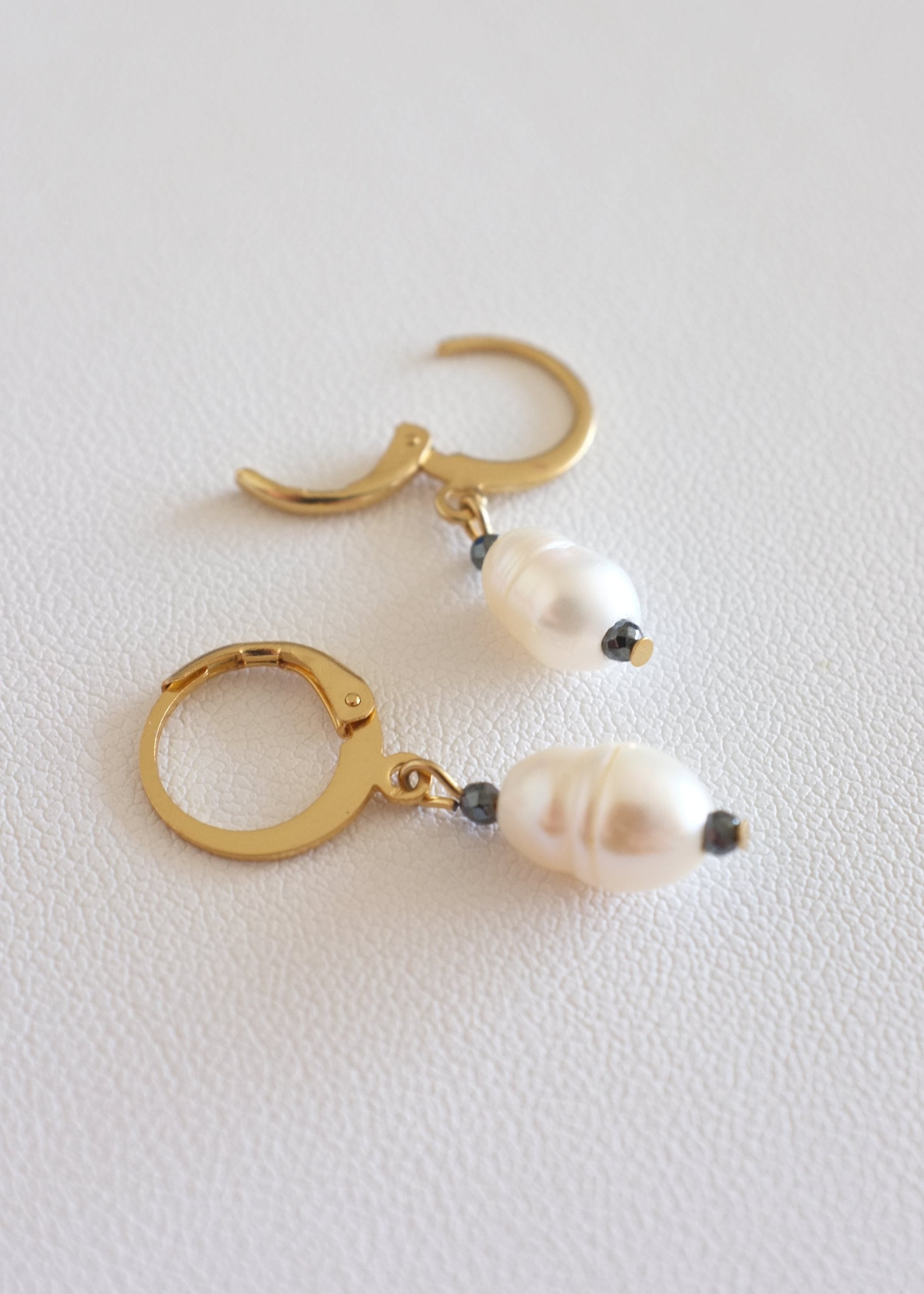 A pair of gold-colored stainless steel hoop earrings with freshwater pearl adornments.