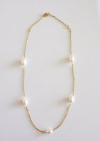 A gold stainless steel necklace with freshwater pearls displayed on a white surface.