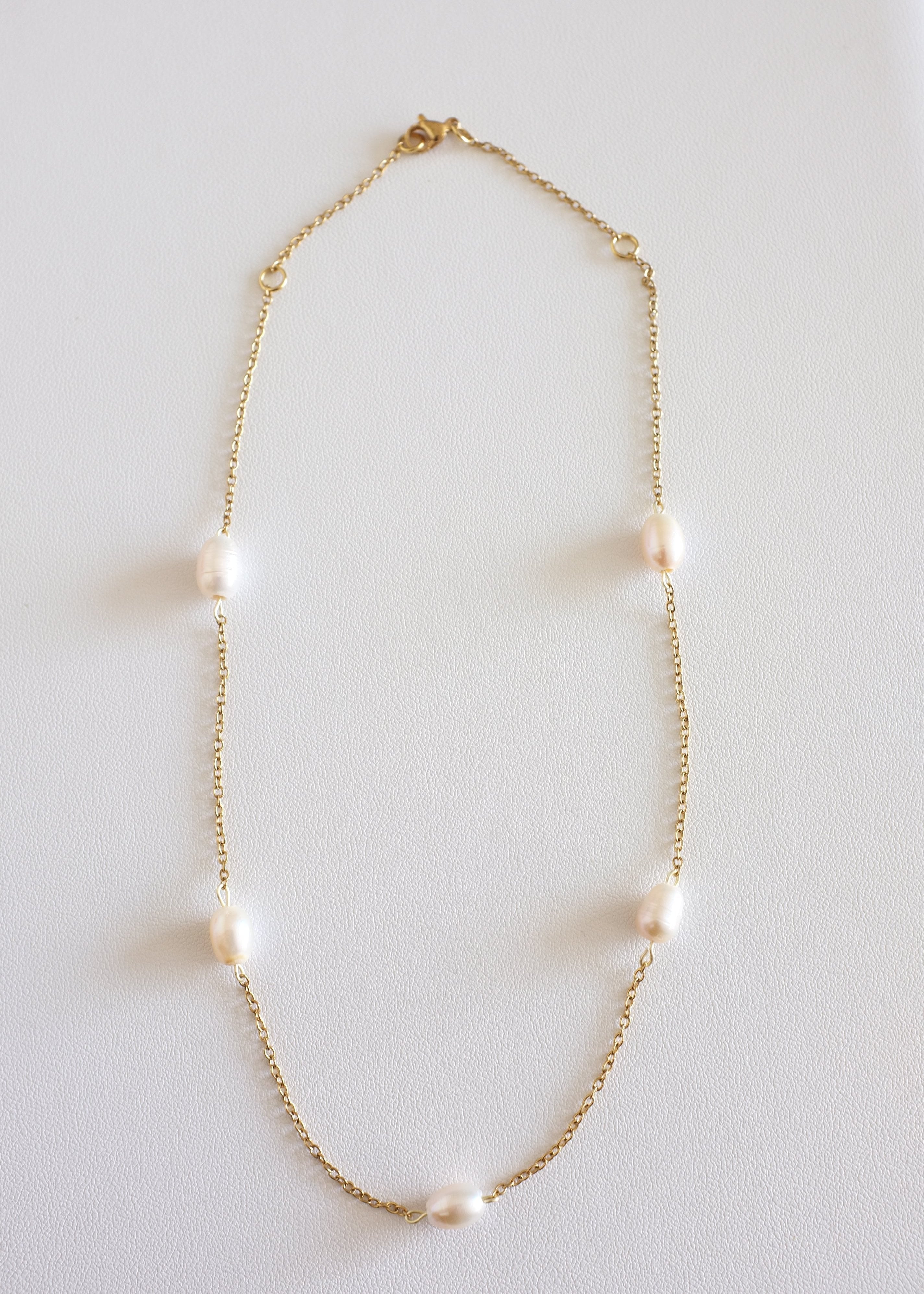 A gold stainless steel necklace with freshwater pearls displayed on a white surface.