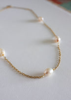 A stainless steel necklace with freshwater pearls displayed on a white surface.