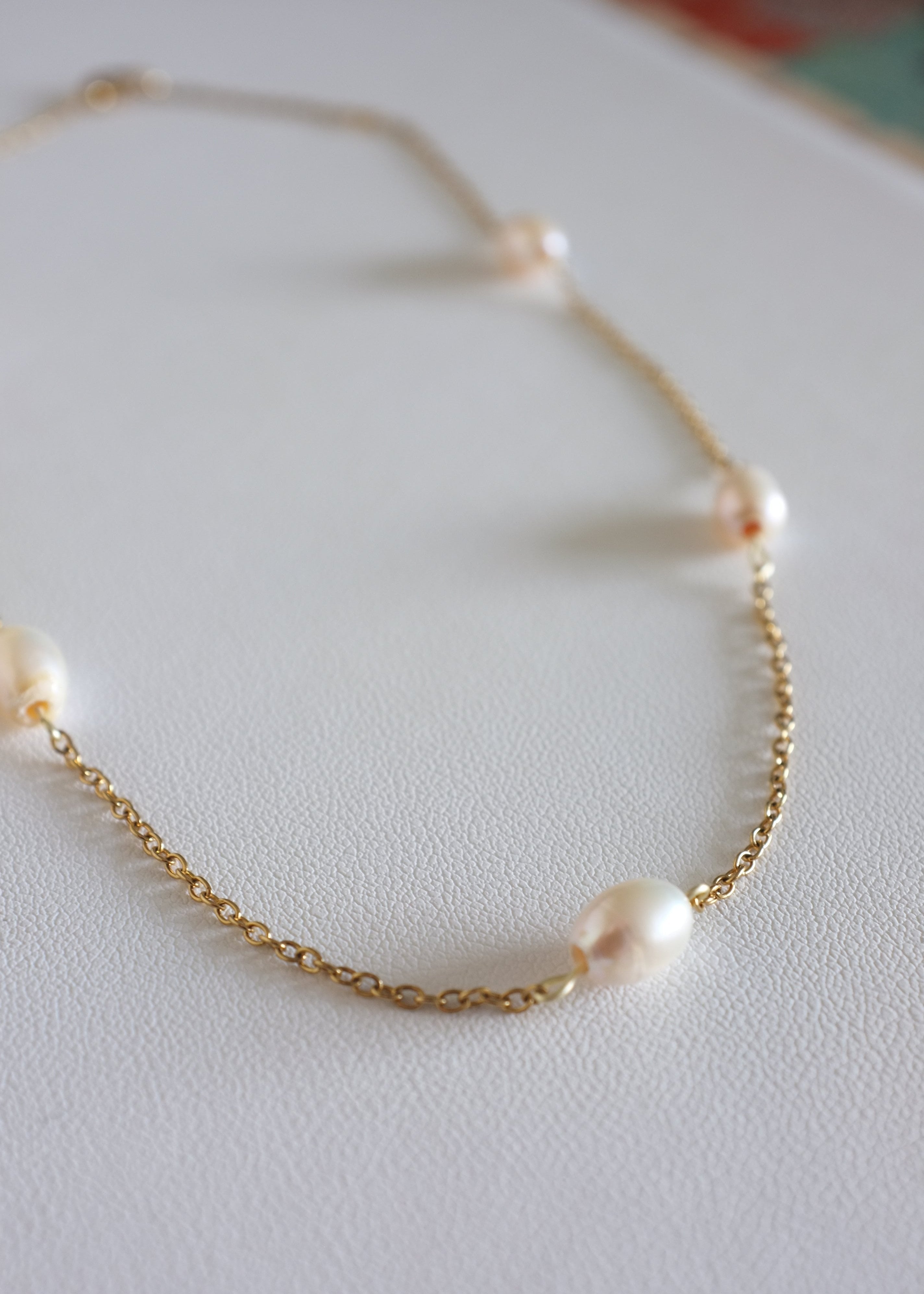 A stainless steel necklace with freshwater pearls displayed on a white surface.