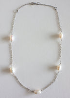 A silver stainless steel necklace with freshwater pearls displayed on a white surface.