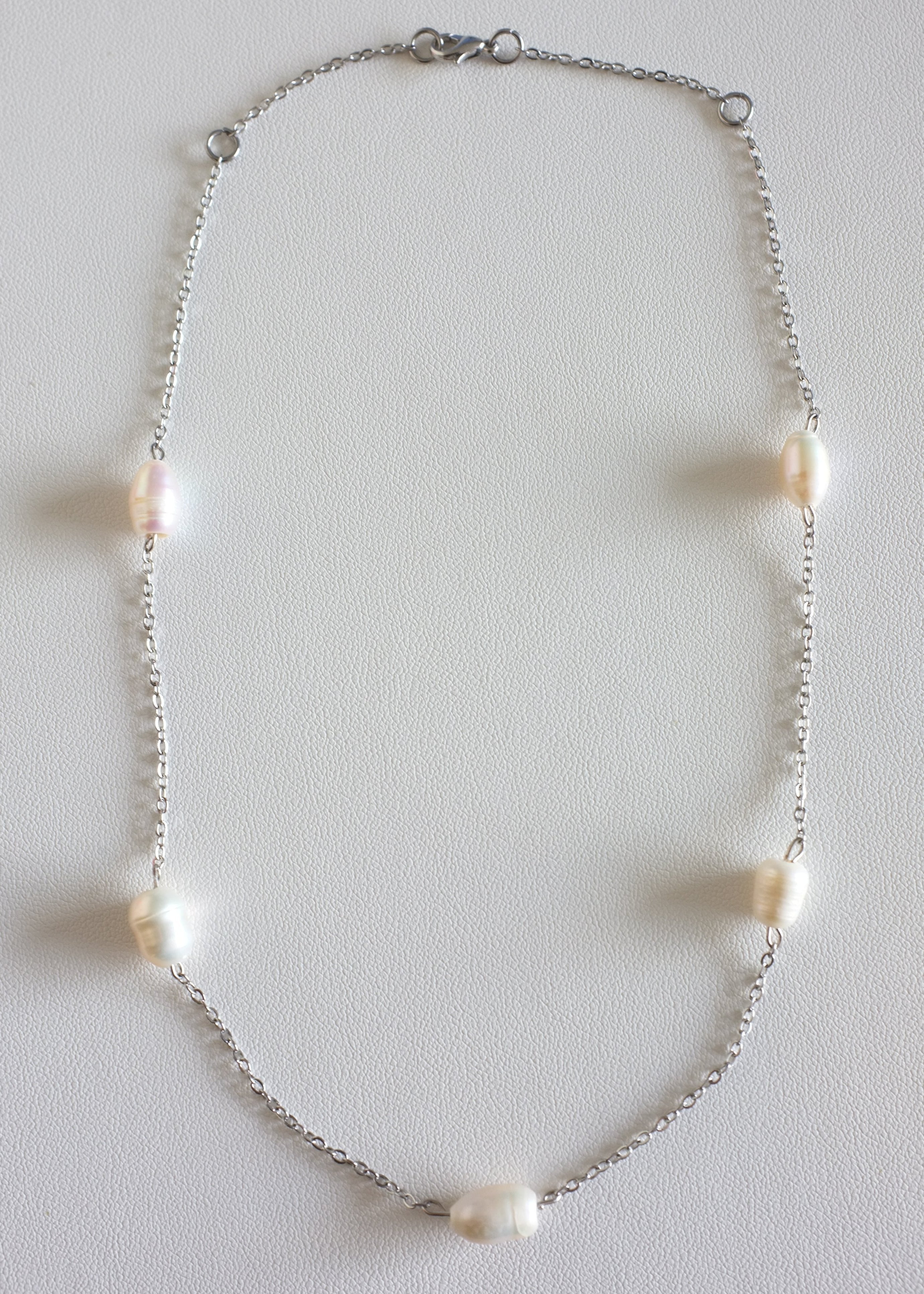 A silver stainless steel necklace with freshwater pearls displayed on a white surface.