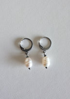 A pair of silver-colored stainless steel hoop earrings with freshwater pearl adornments on white background