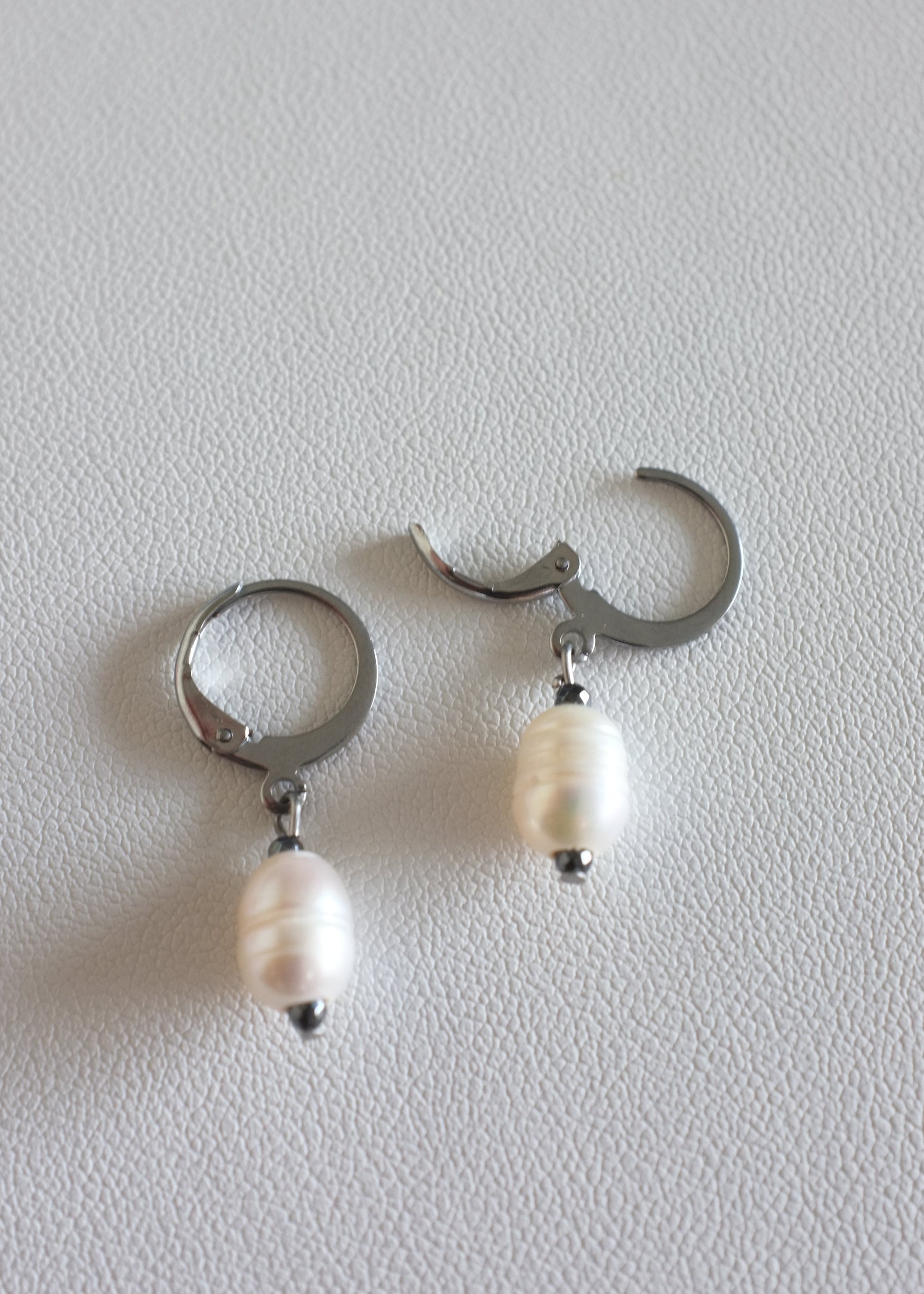 A pair of silver-colored stainless steel hoop earrings with freshwater pearl adornments.