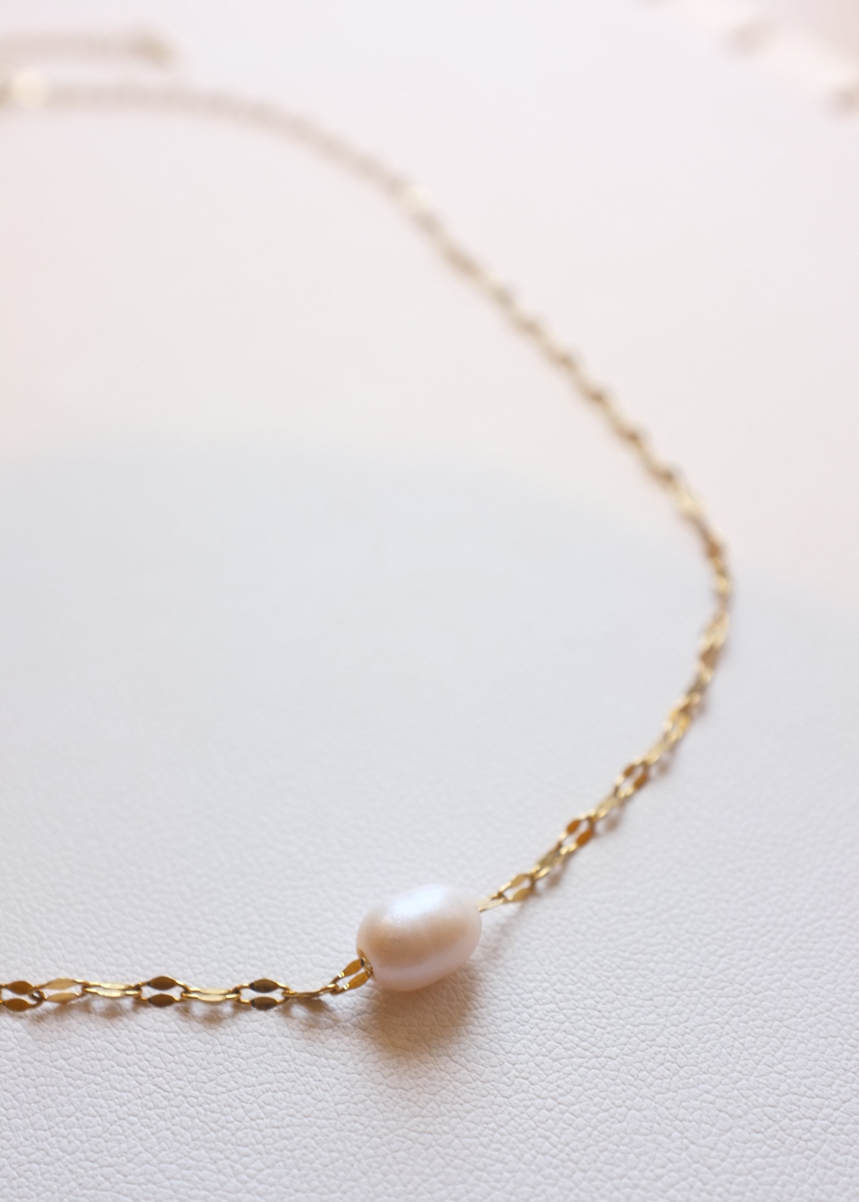 close up of gold stainless steel chain with freshwater pearl on white background