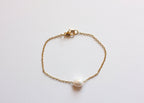 Gold stainless steel chain bracelet with a single freshwater pearl on white background