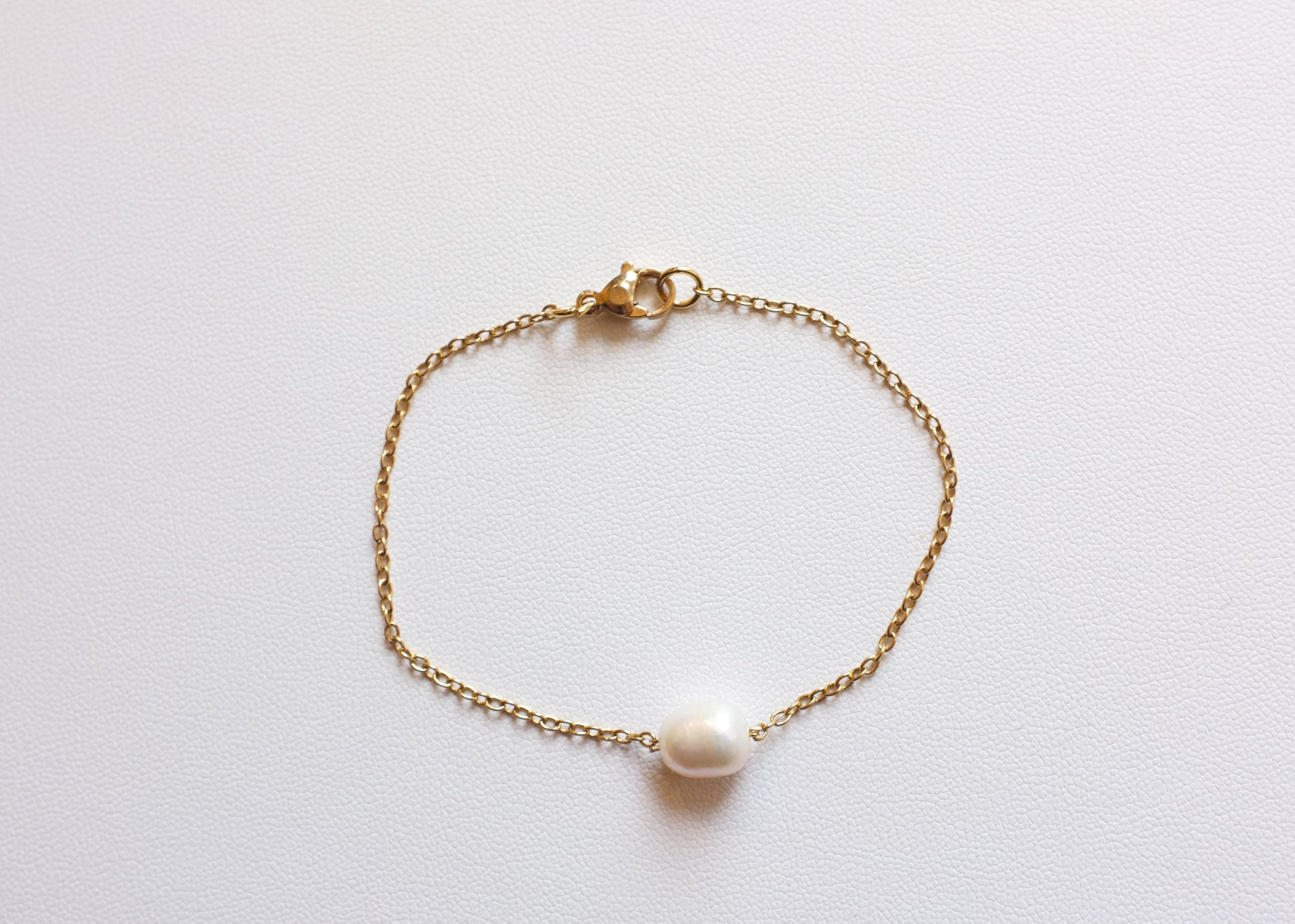 Gold stainless steel chain bracelet with a single freshwater pearl on white background
