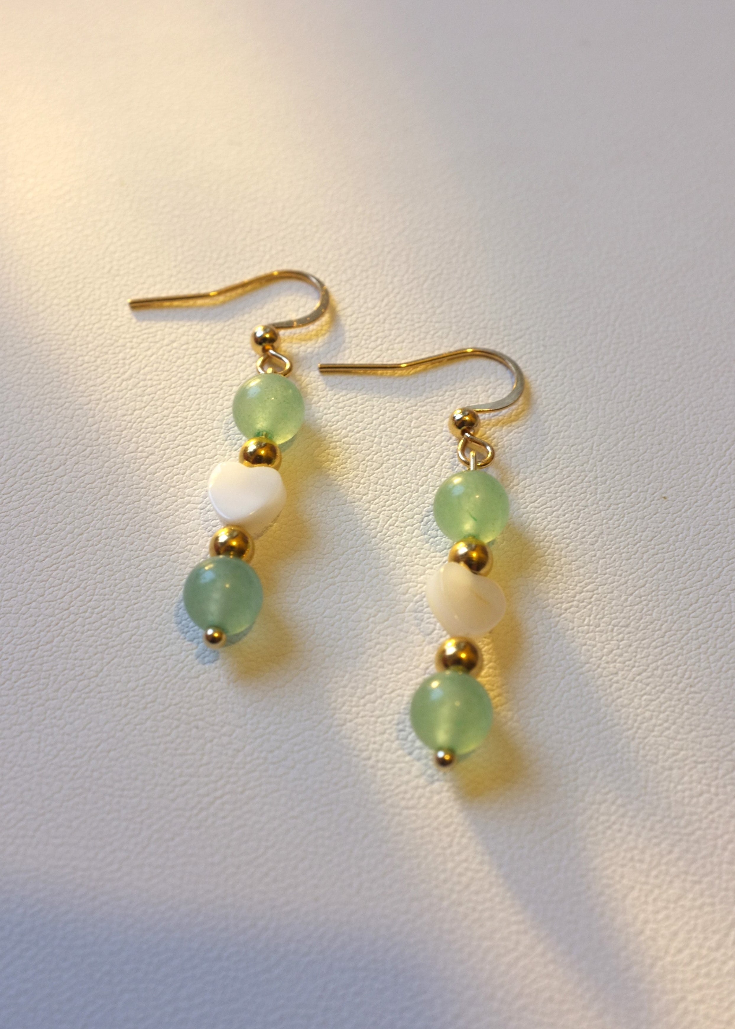 A pair of earrings featuring green aventurine stones and gold-colored accents on a light background.