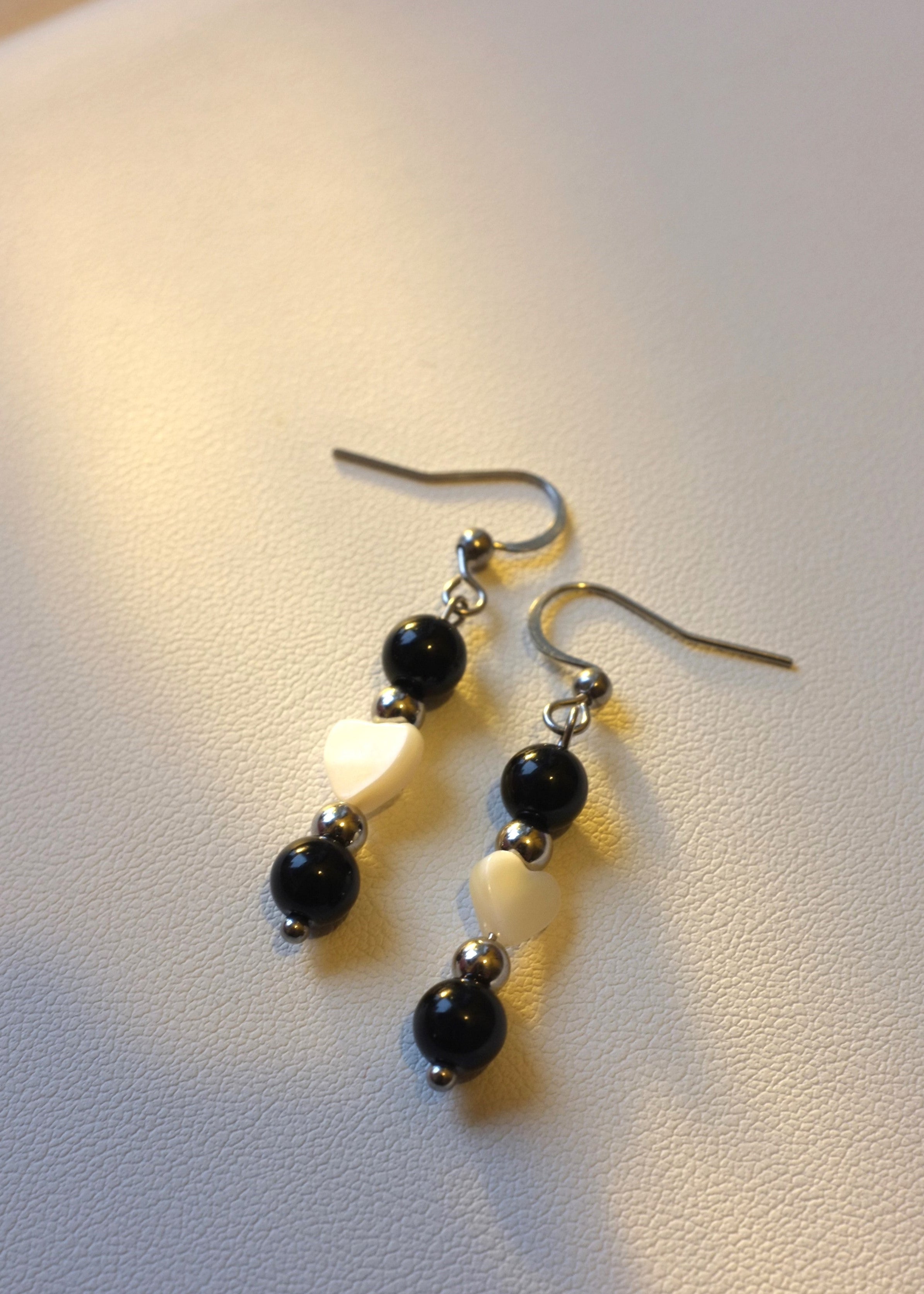 A pair of onyx stone earrings with heart-shaped shell accents, displayed on a white surface.