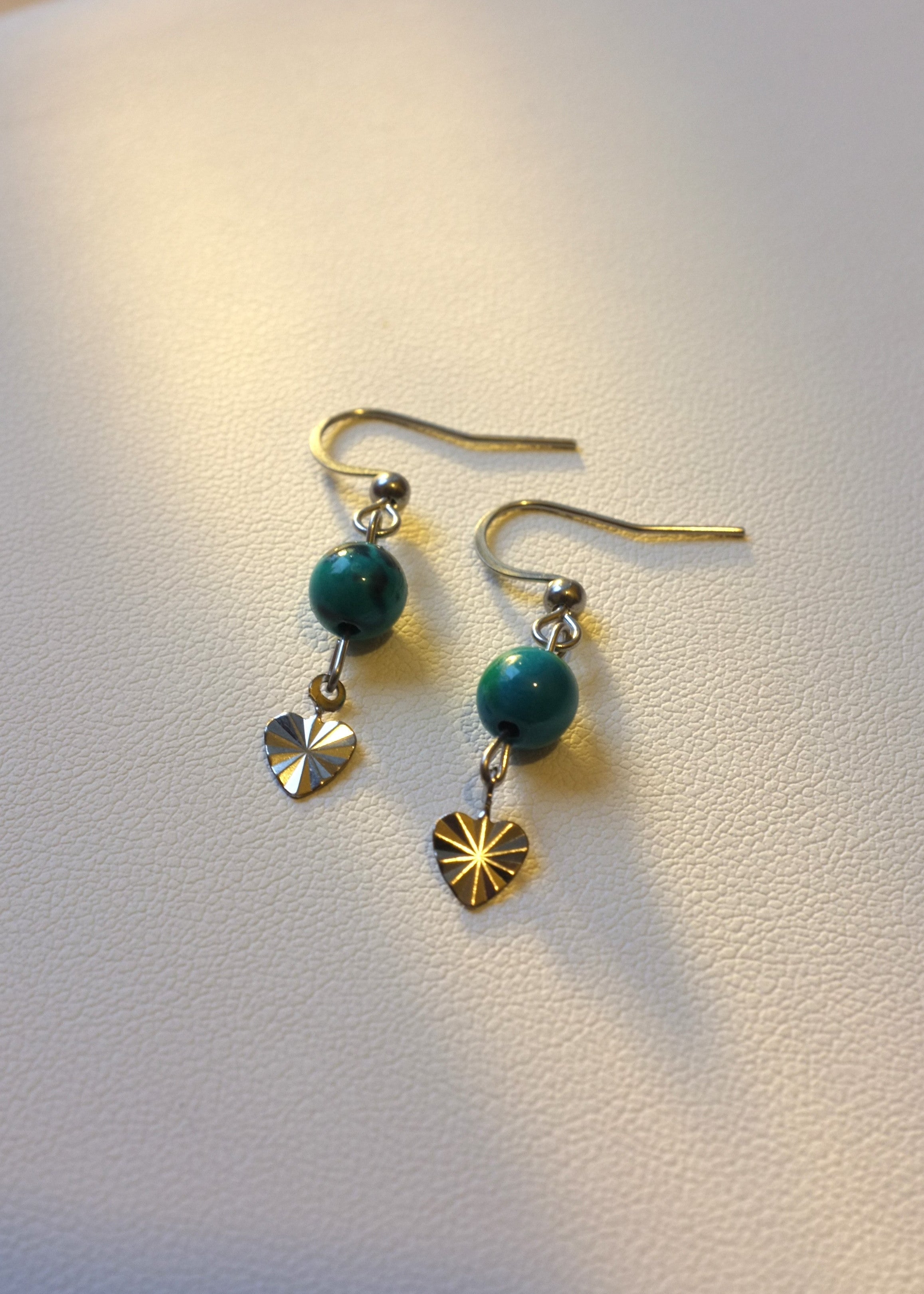 A pair of blue earrings with heart-shaped stainless steel charms, displayed against a white background.