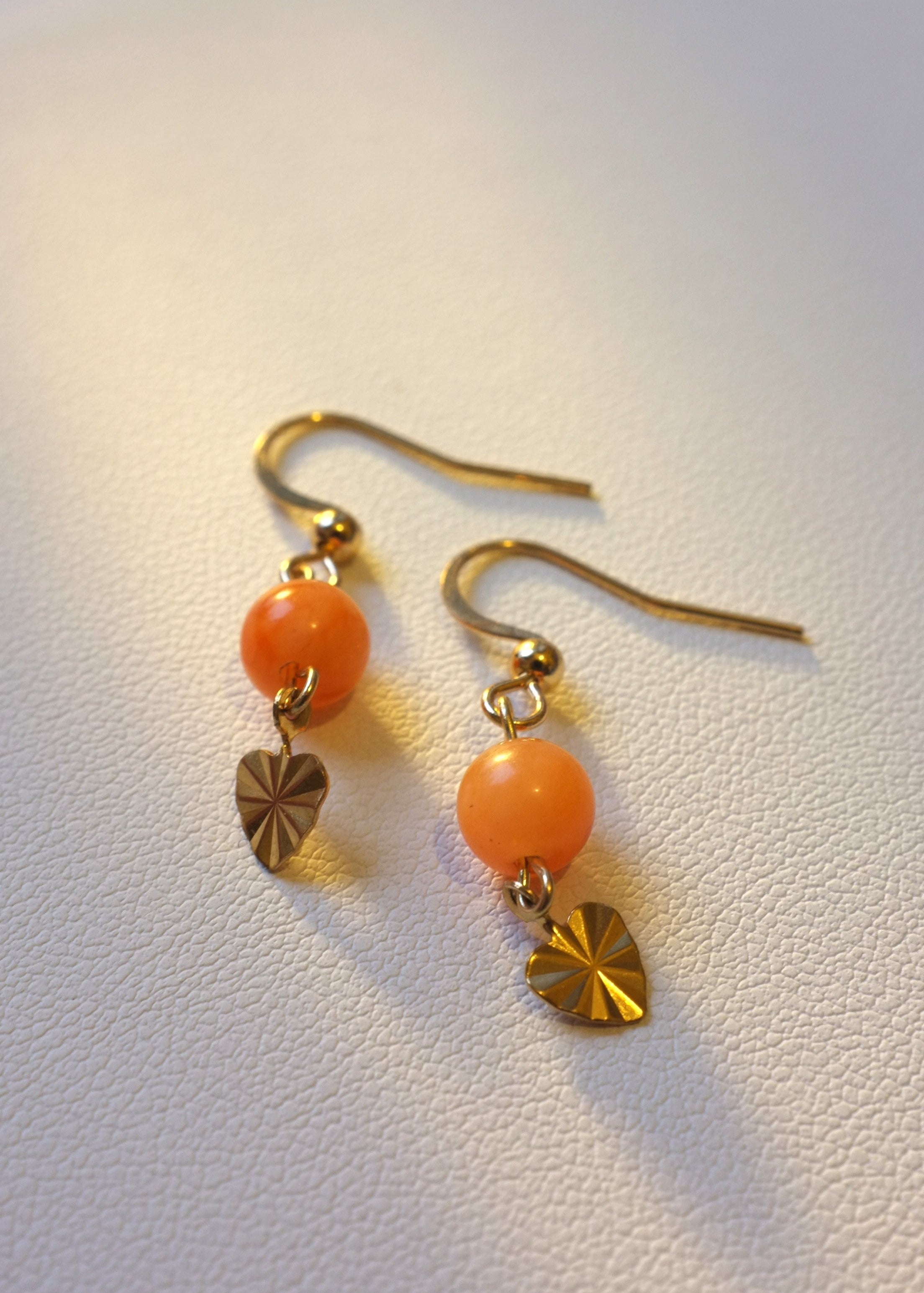 A pair of earrings featuring orange-colored beads and gold-colored thread with heart-shaped charms.