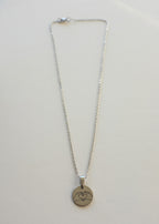 A stainless steel chain necklace with a round medal engraved with a heart symbol, displayed on a white background.