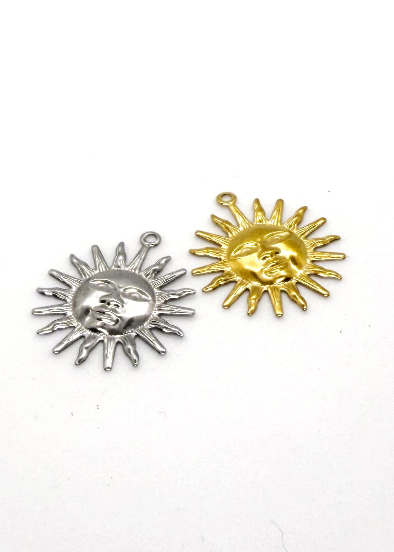 Silver and gold stainless steel sun-shaped charms on a white background