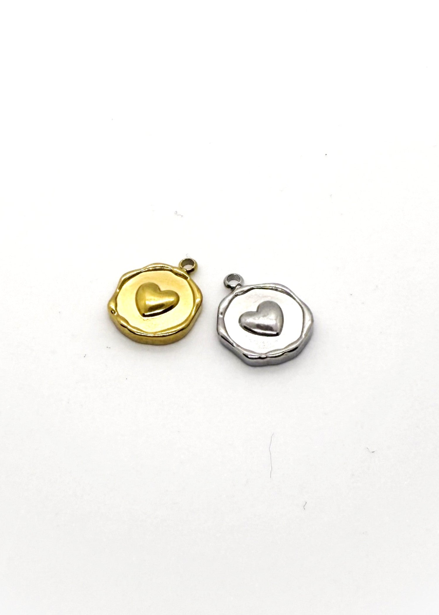 Two stainless steel heart-shaped charms, one gold and one silver, on a white background.